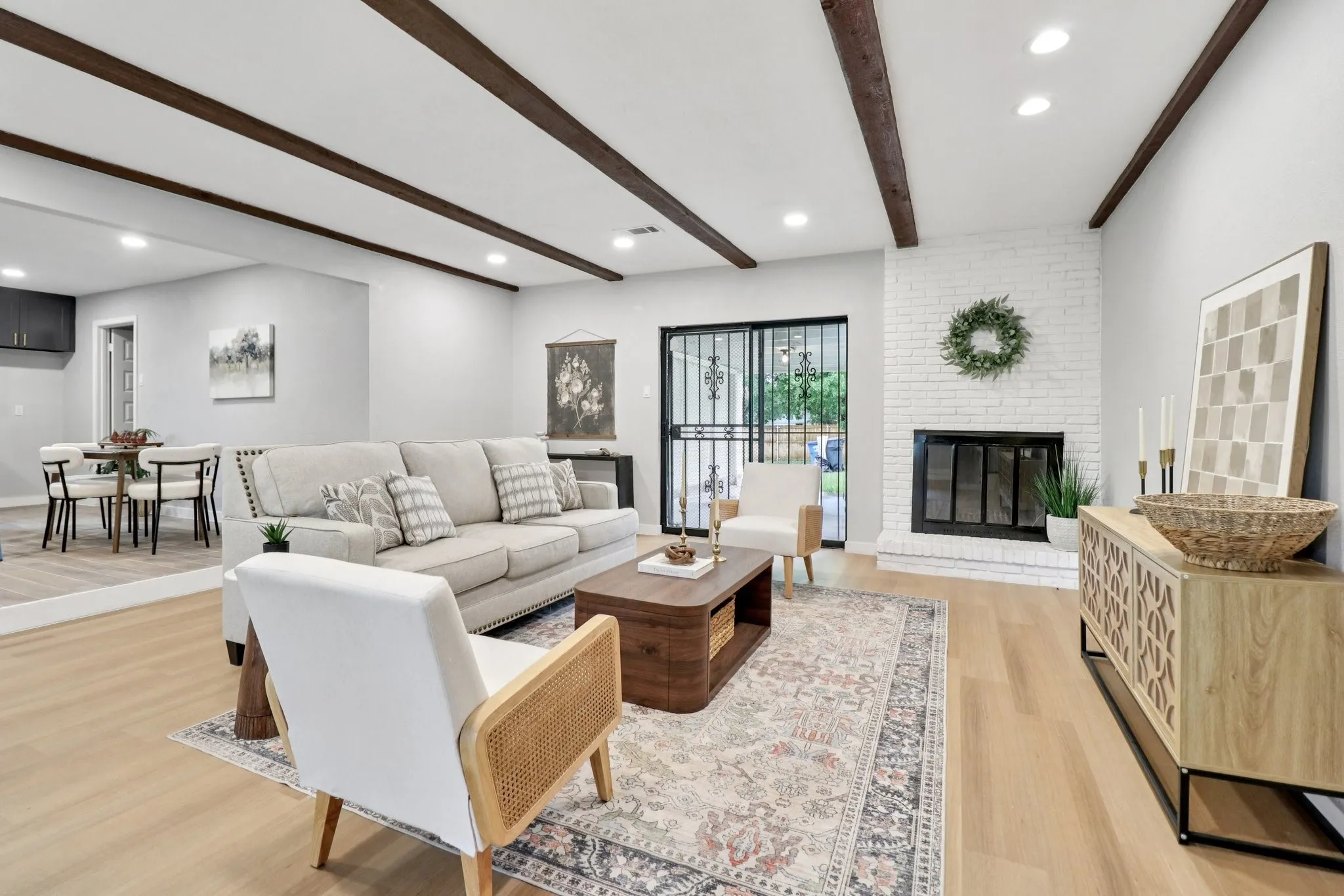 Spacious living area featuring wood-finish flooring, exposed ceiling beams, recessed lighting, and a white-painted brick fireplace