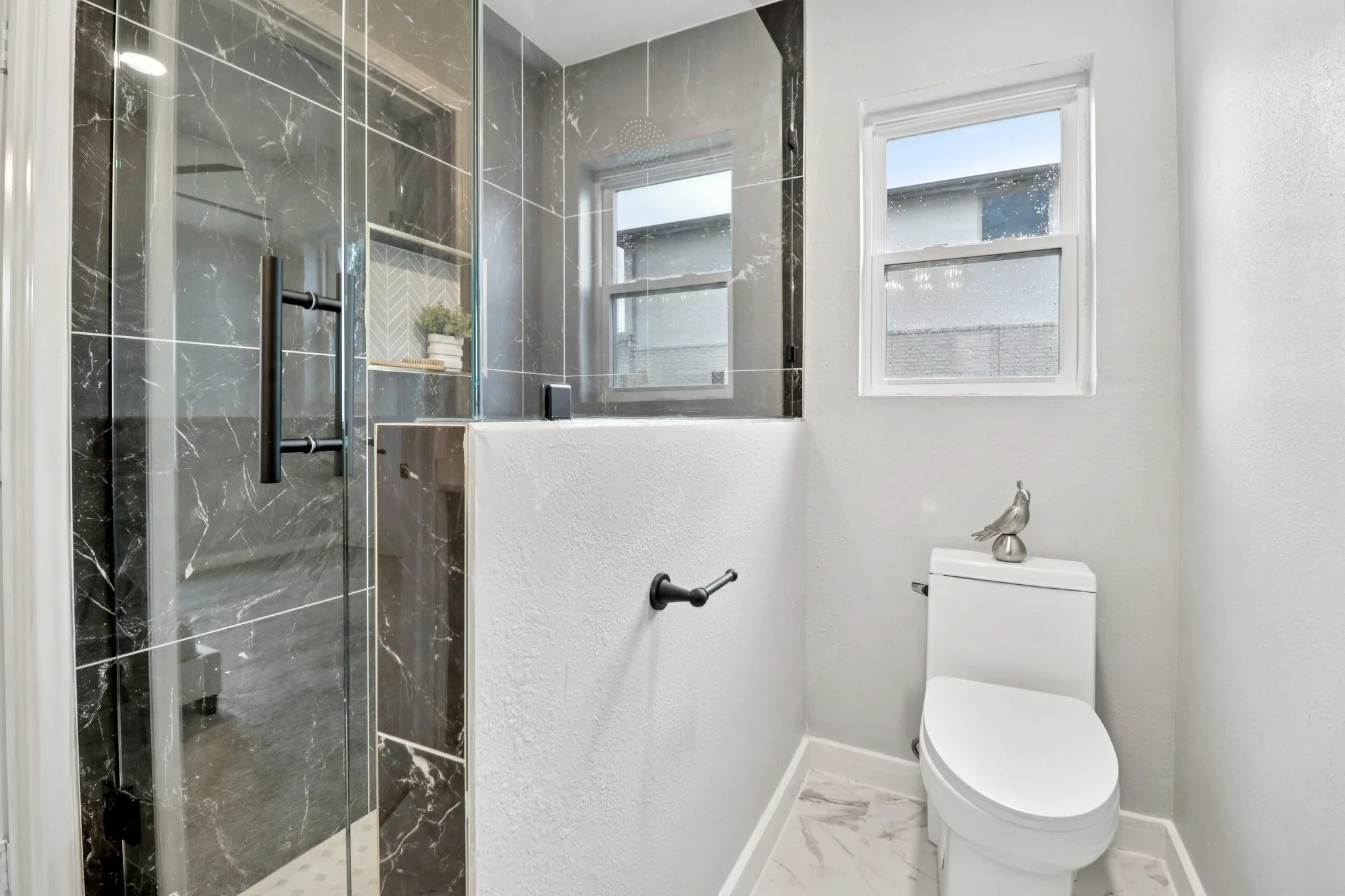 Glass-enclosed shower featuring dark marble-look tile, matte black hardware, and a built-in niche with herringbone accent tile