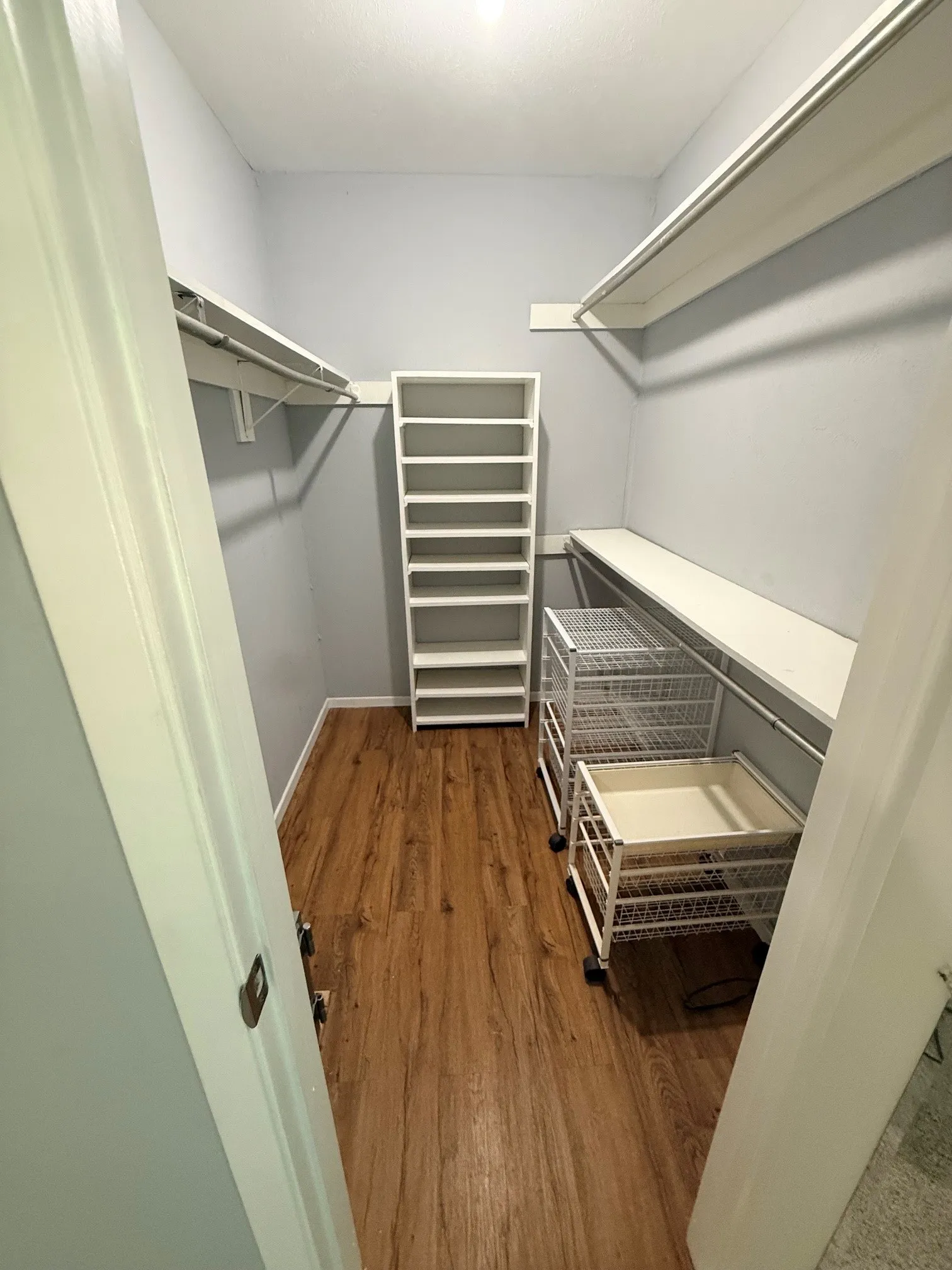 Walk-in closet featuring wood-finish flooring, light gray walls, and white shelving units