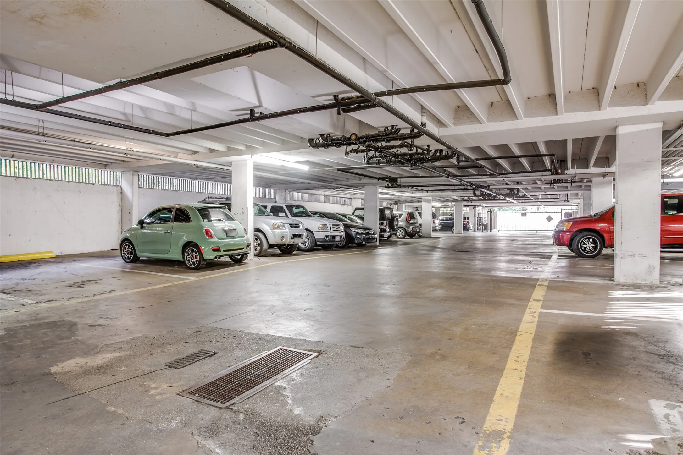 Underground parking garage featuring concrete flooring, exposed overhead piping, and integrated lighting fixtures