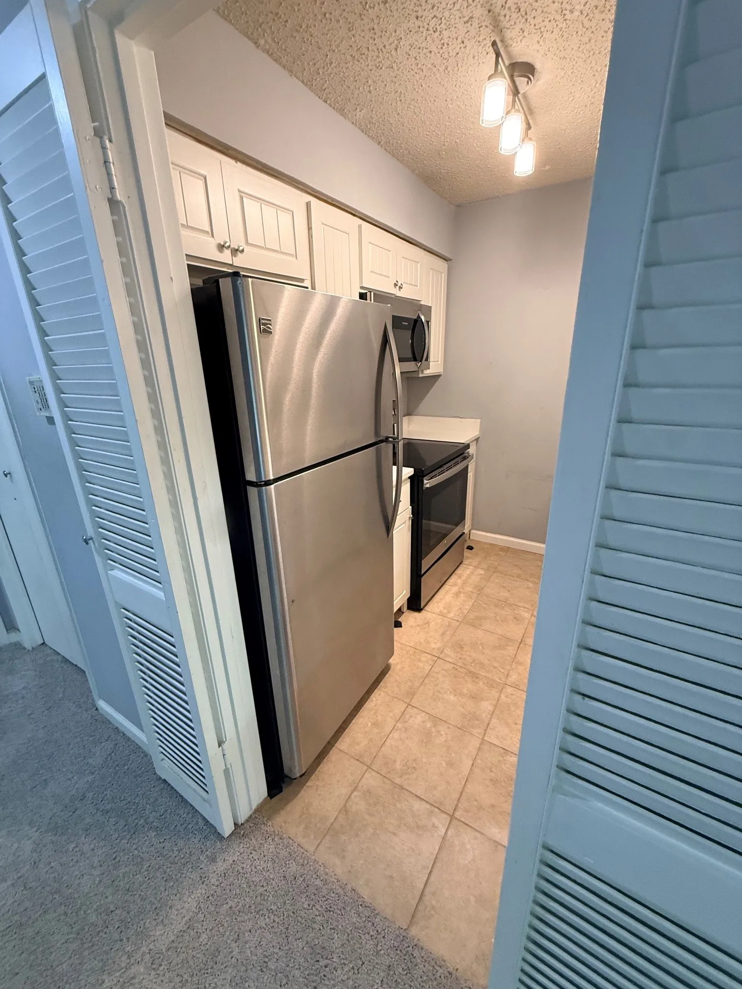 Kitchenette featuring stainless steel appliances, light-colored cabinetry, track lighting, and tile flooring