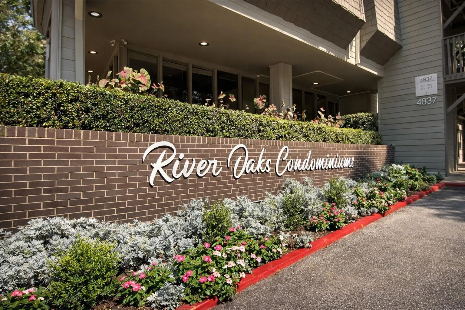 Brick facade with integrated signage, featuring a manicured hedge and diverse landscaping with flowering plants