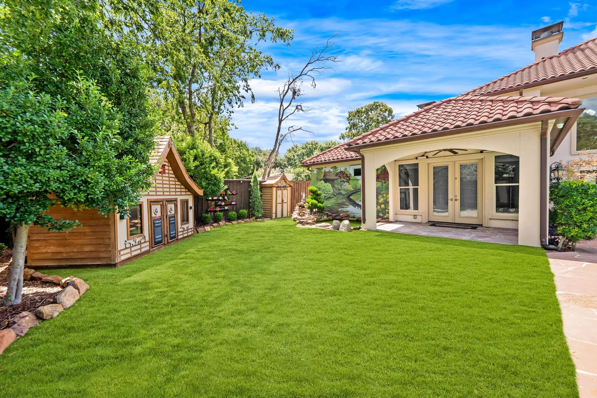 Expansive private backyard featuring a lush lawn, mature trees, a covered patio with double French doors, and a decorative garden structure