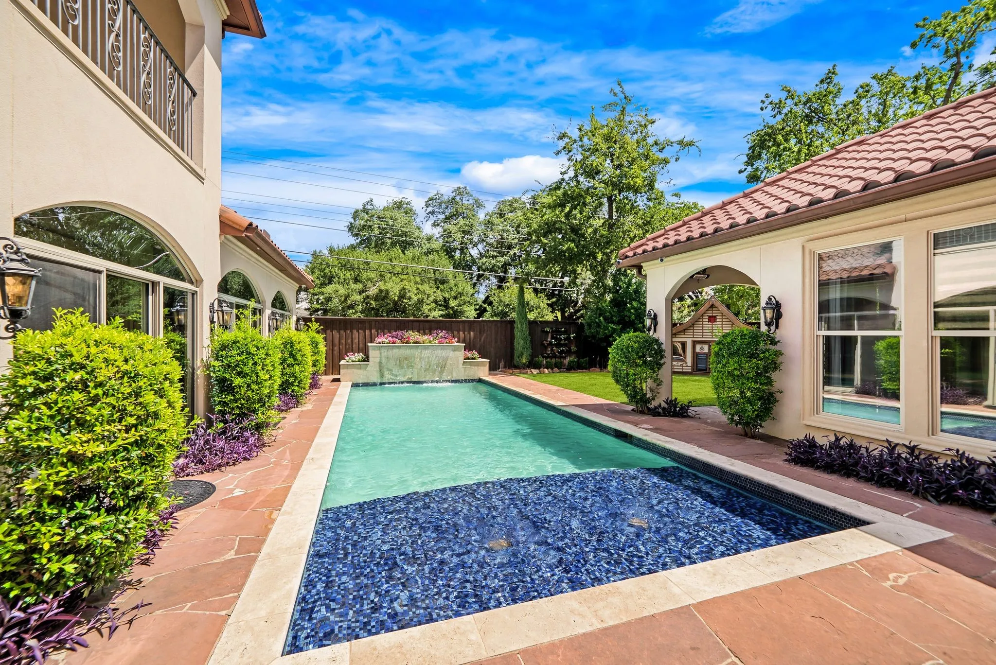 Inviting backyard oasis featuring a rectangular swimming pool with integrated spa, stone coping, and a waterfall feature