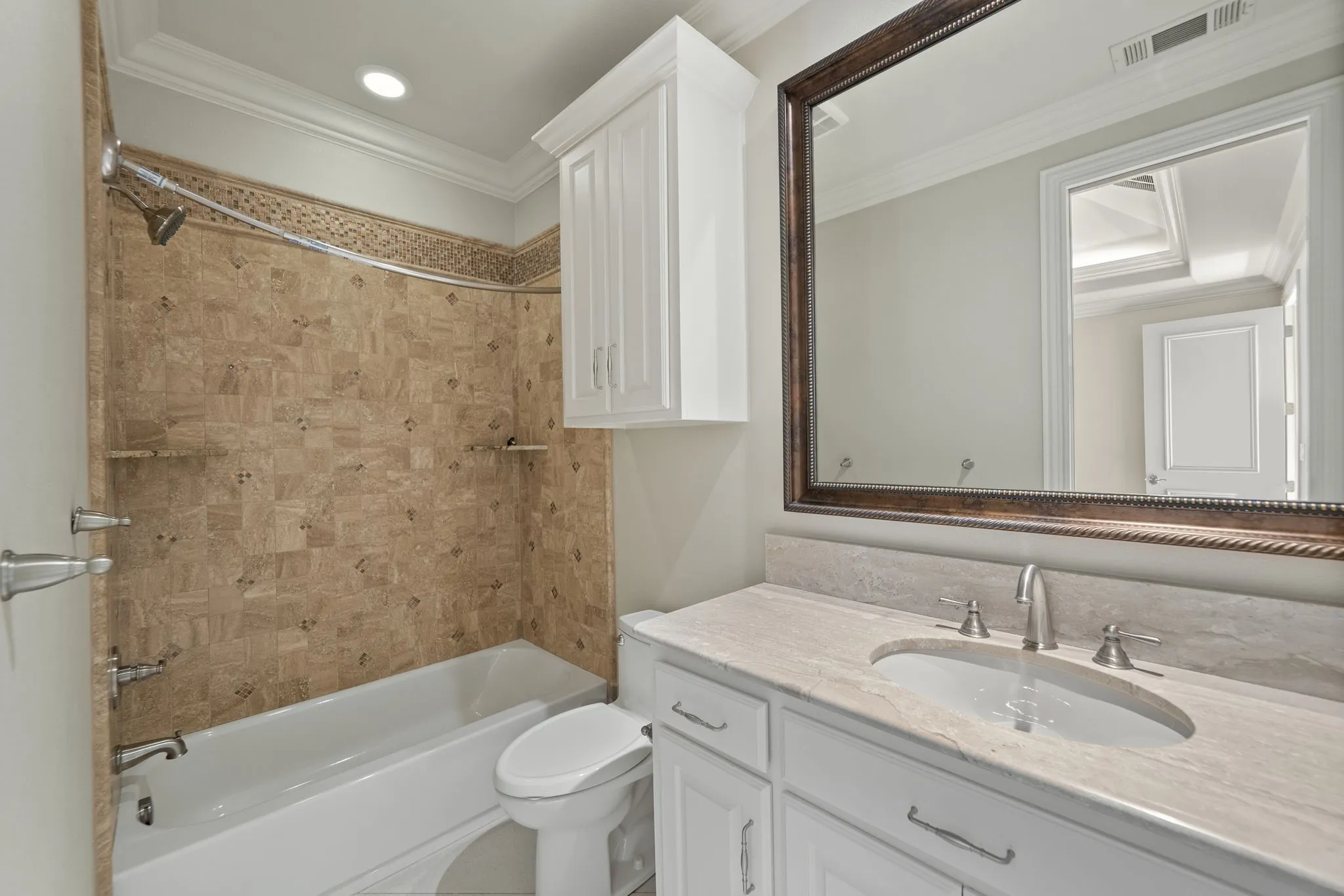 Bathroom featuring a bathtub with a tiled surround, a white vanity with a stone countertop, an undermount sink, and a framed mirror