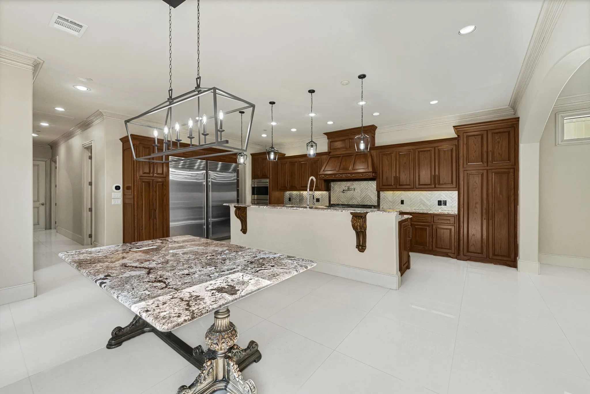 Kitchen featuring custom wood cabinetry, a large center island with corbel accents, a patterned tile backsplash, stainless steel appliances, and recessed lighting