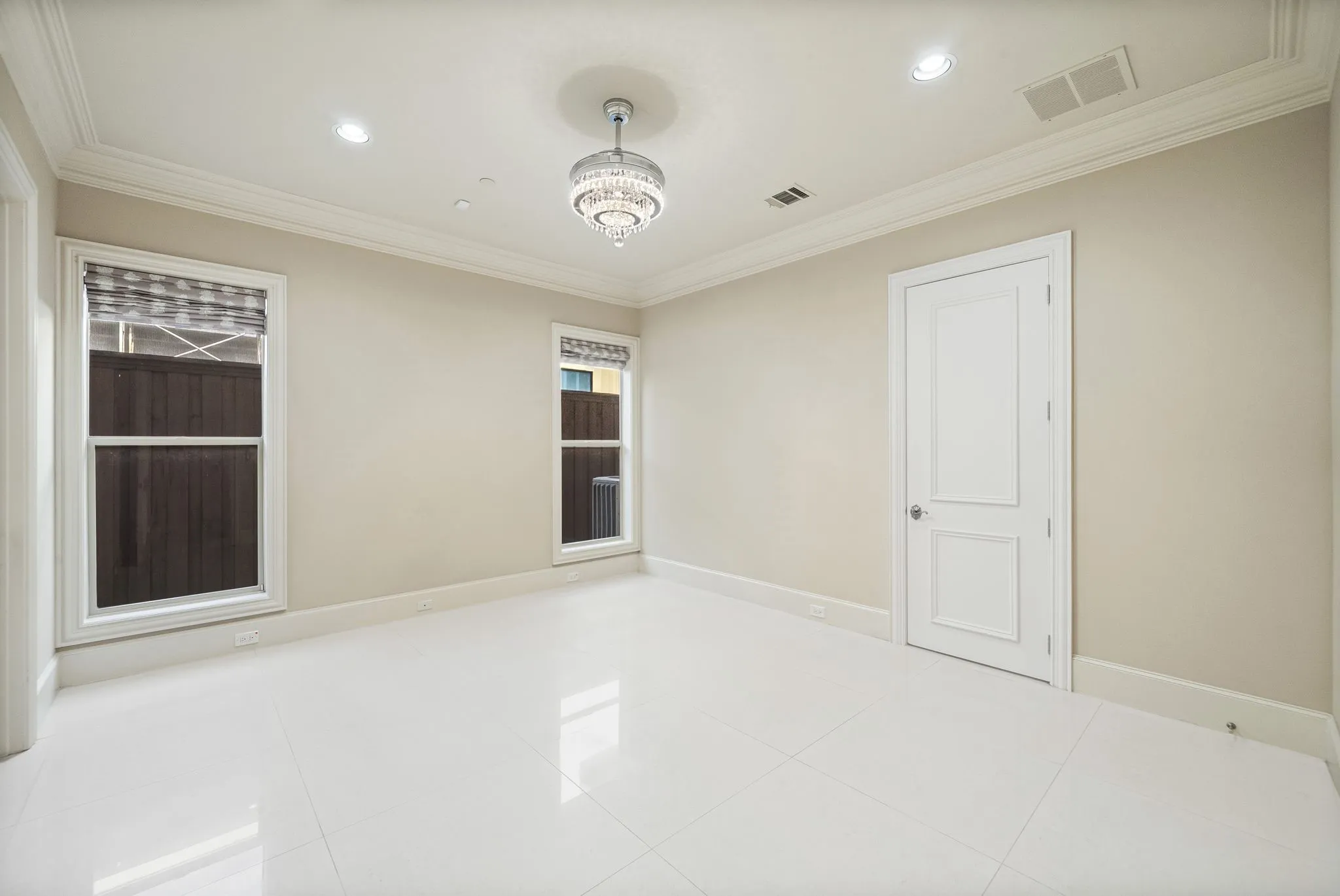 Spacious room featuring white tile flooring, crown molding, a two-panel interior door, and a tiered crystal chandelier