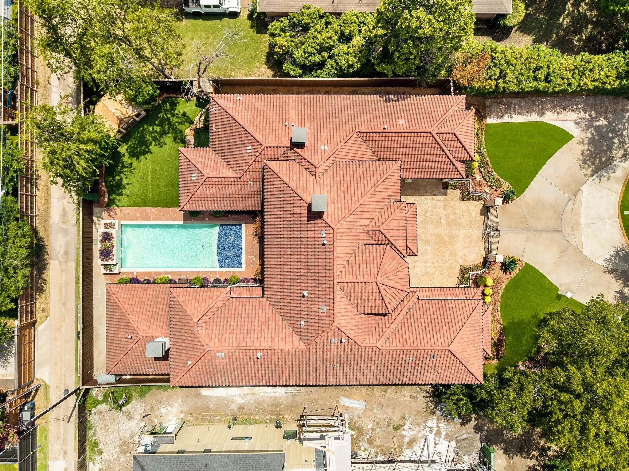 Tile roof architecture featuring a geometric swimming pool, extensive paved patio, a circular driveway, and manicured landscaping