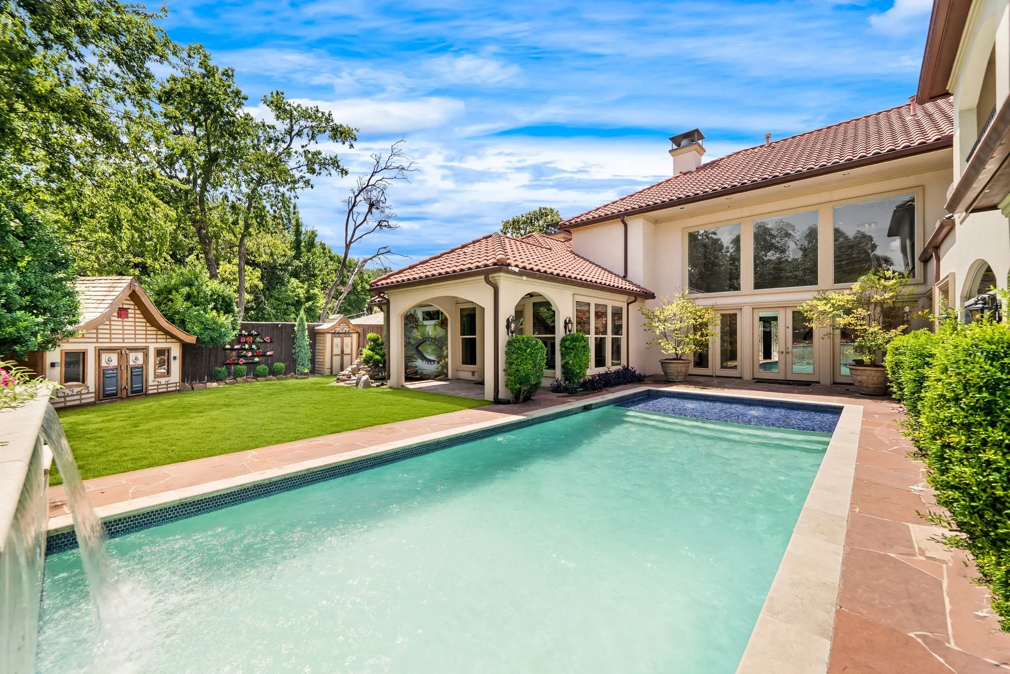 Exterior featuring a large swimming pool with a waterfall feature, expansive lawn, tile roof, multiple large windows, and a covered patio area
