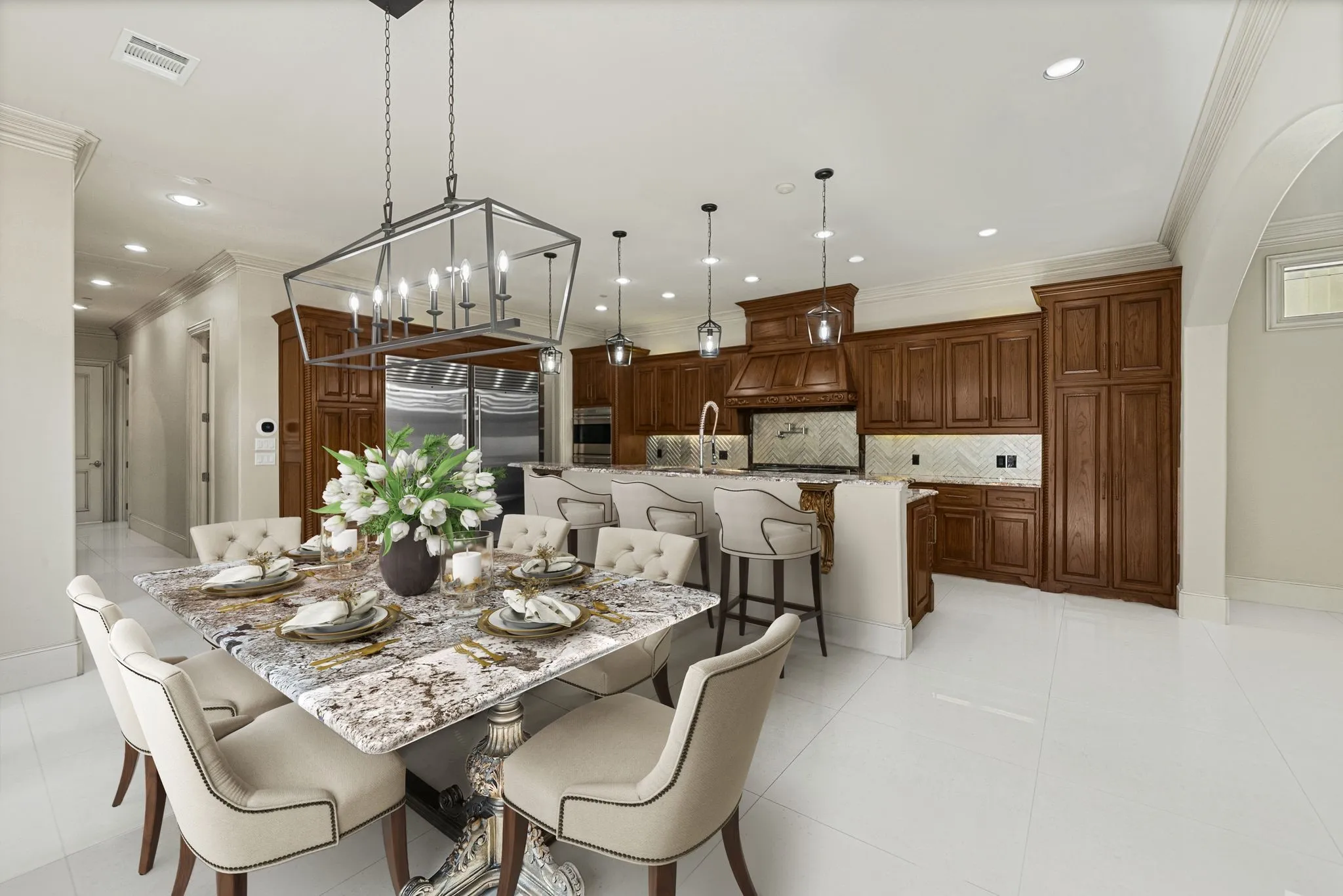 Spacious open-concept kitchen and dining area featuring wood cabinetry, stainless steel appliances, a center island with bar seating, and a large dining table under a statement chandelier