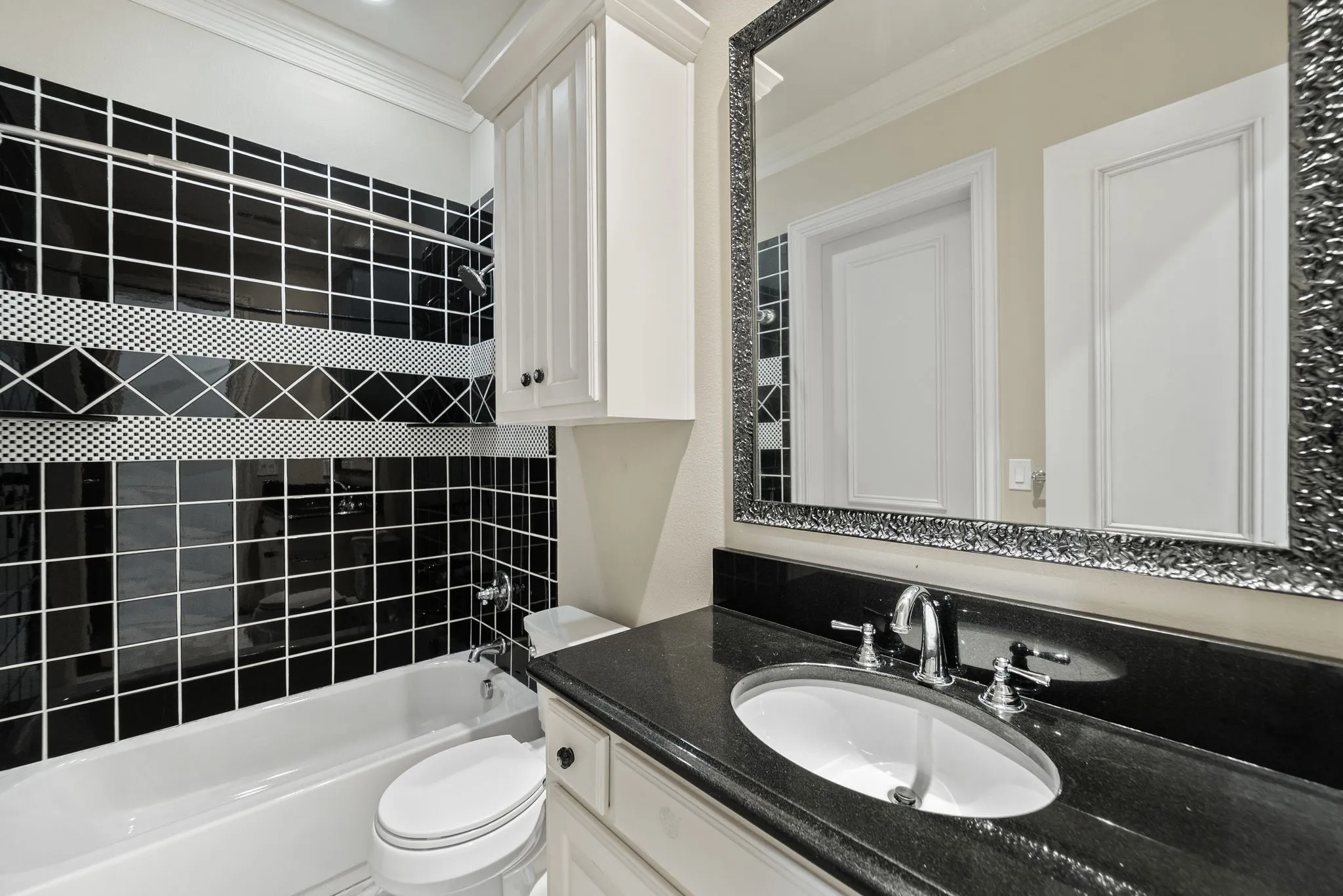 Bathroom featuring a black tile shower surround with decorative accent bands, a white bathtub, and a built-in vanity