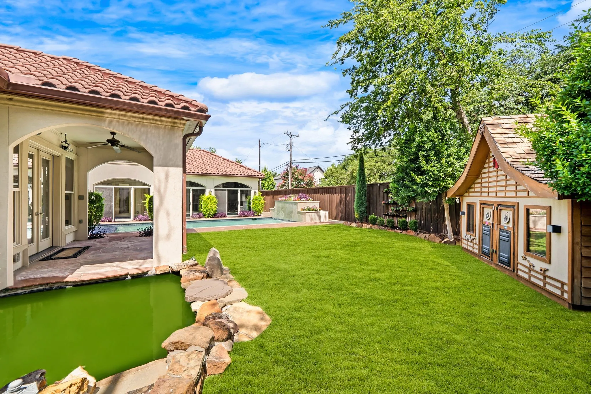 Expansive backyard featuring a green lawn, a rock-lined water feature, and a custom playhouse