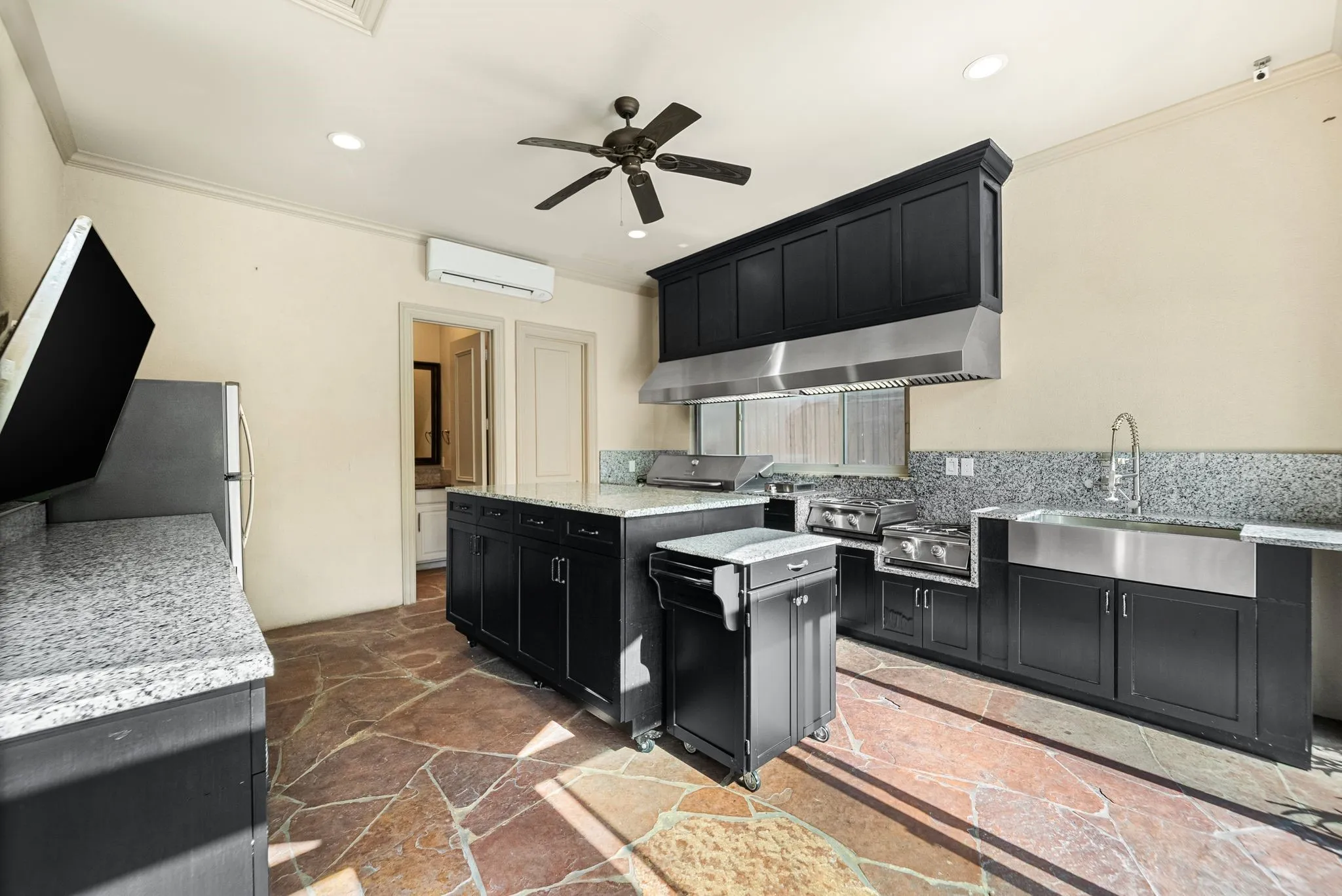 Outdoor kitchen featuring black cabinetry, granite countertops, a stainless steel farmhouse sink, and flagstone flooring