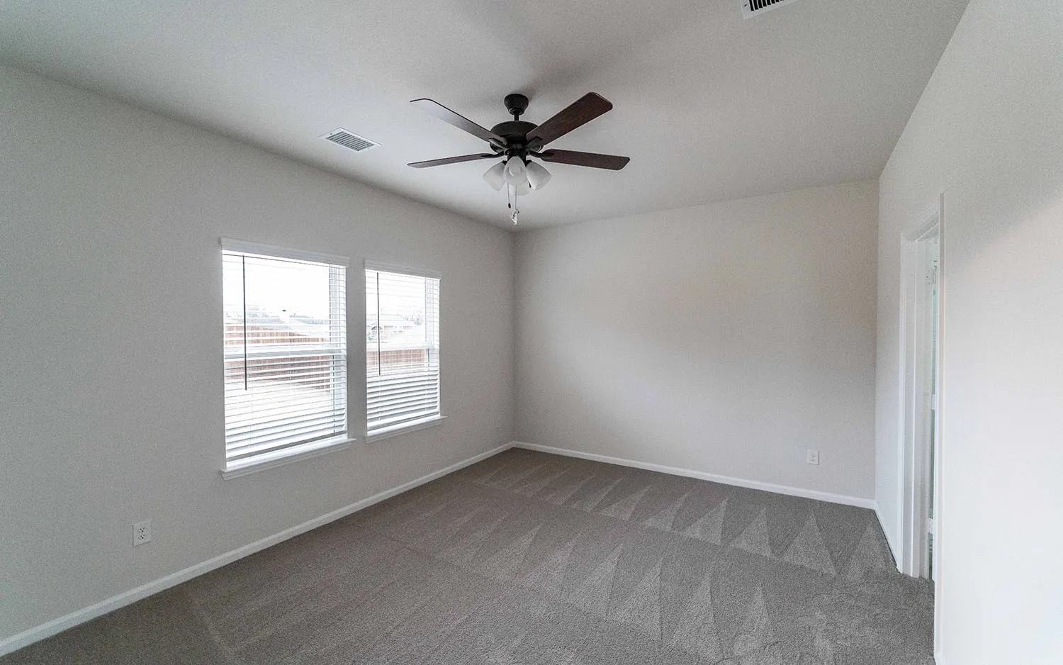Spacious room featuring neutral carpeting, a ceiling fan with integrated lighting, and two windows with blinds
