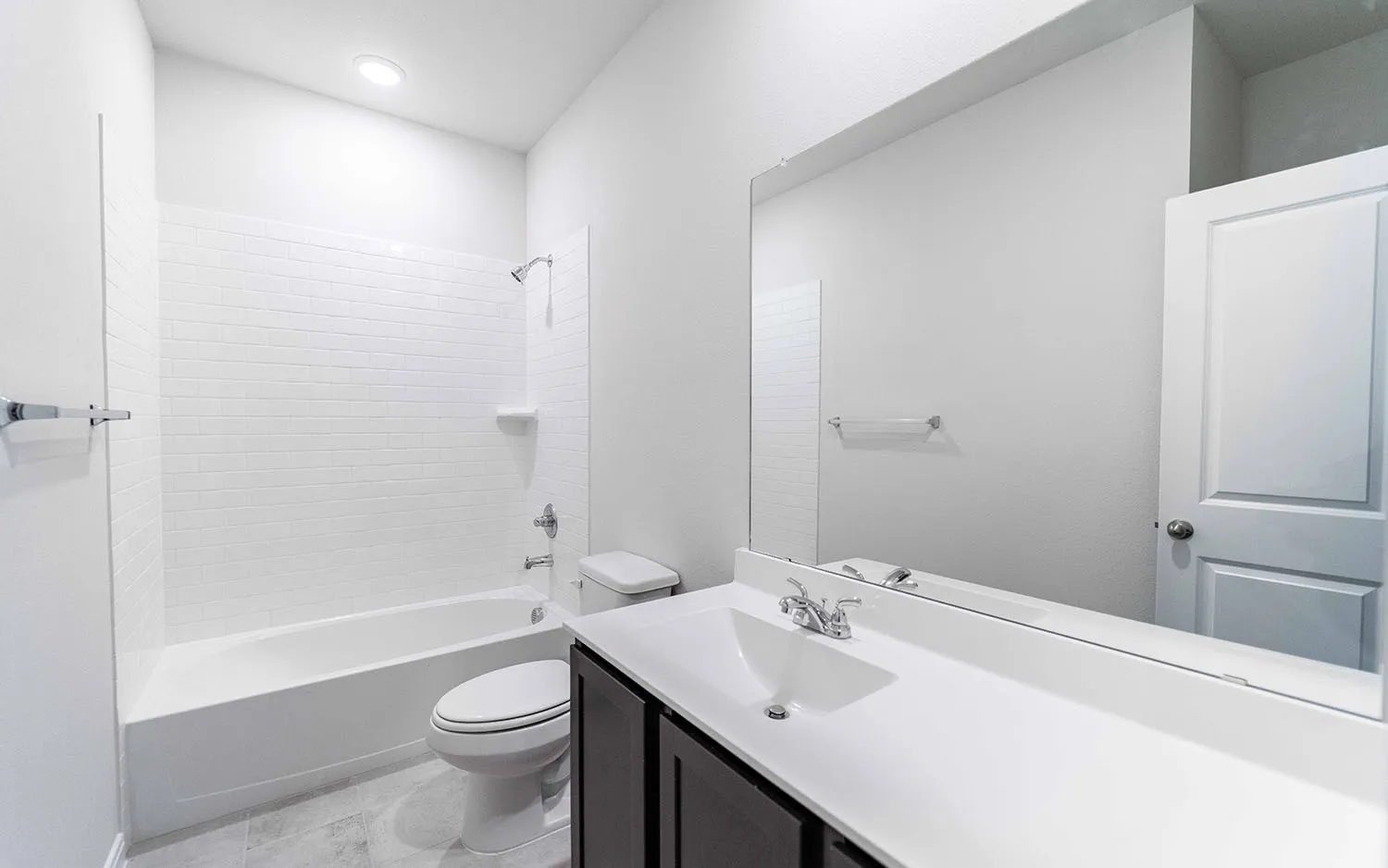 Bathroom featuring a wood-finish vanity with an integrated sink, a large wall-mounted mirror, and white subway tile surrounding the tub
