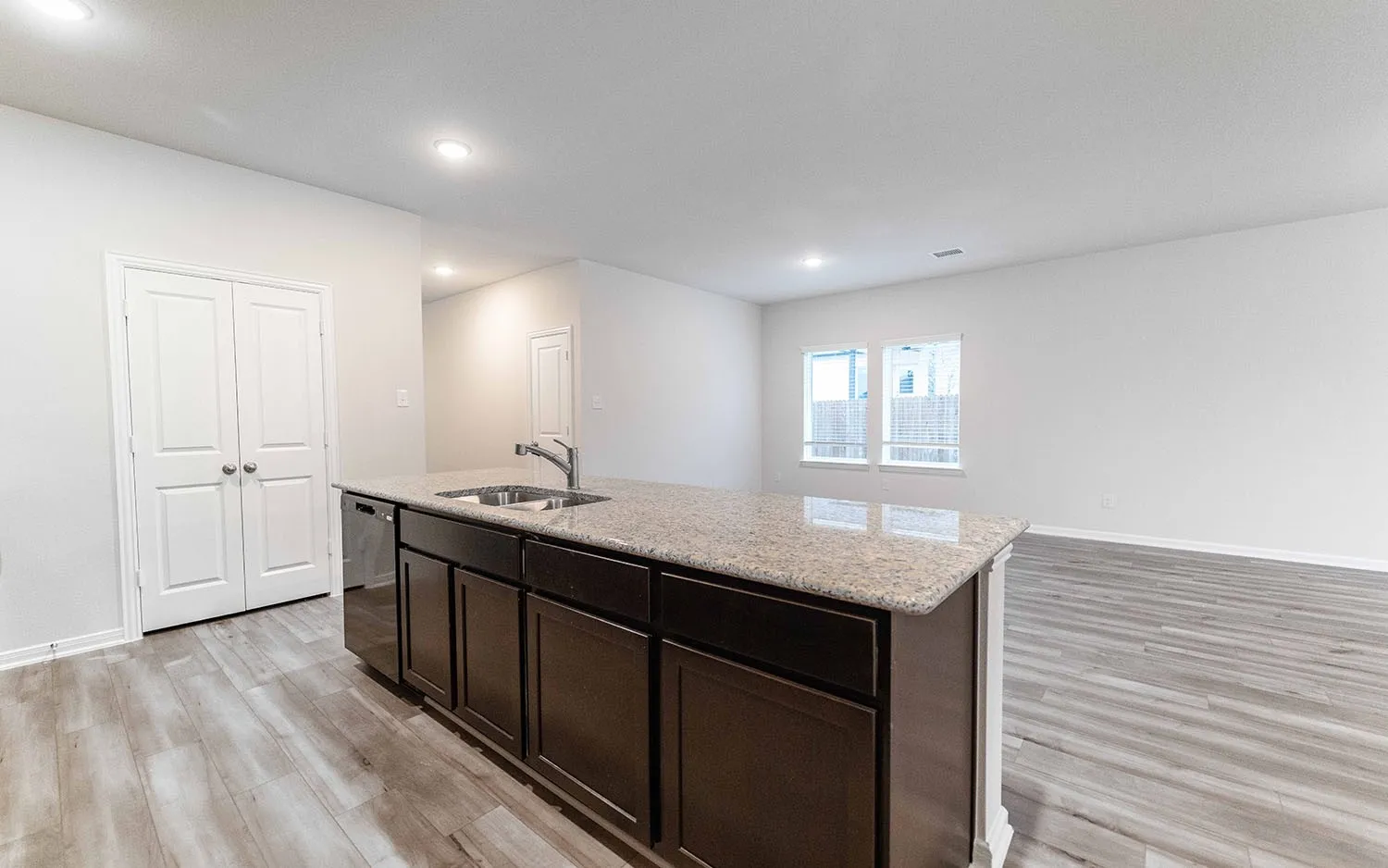 Kitchen island featuring a stainless steel sink with a high-arc faucet, integrated dishwasher, and dark wood-finish cabinetry