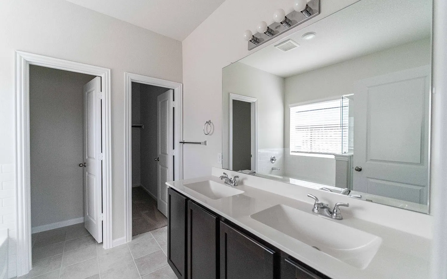Bathroom featuring a dual vanity with rectangular undermount sinks, dark wood-finish cabinetry, and a full-width mirror