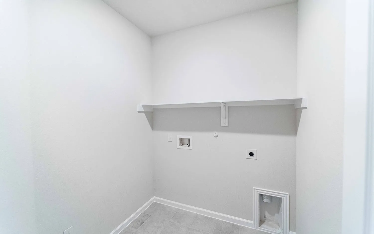Laundry area featuring tile flooring, white baseboards, a wall-mounted shelf, and appliance hookups
