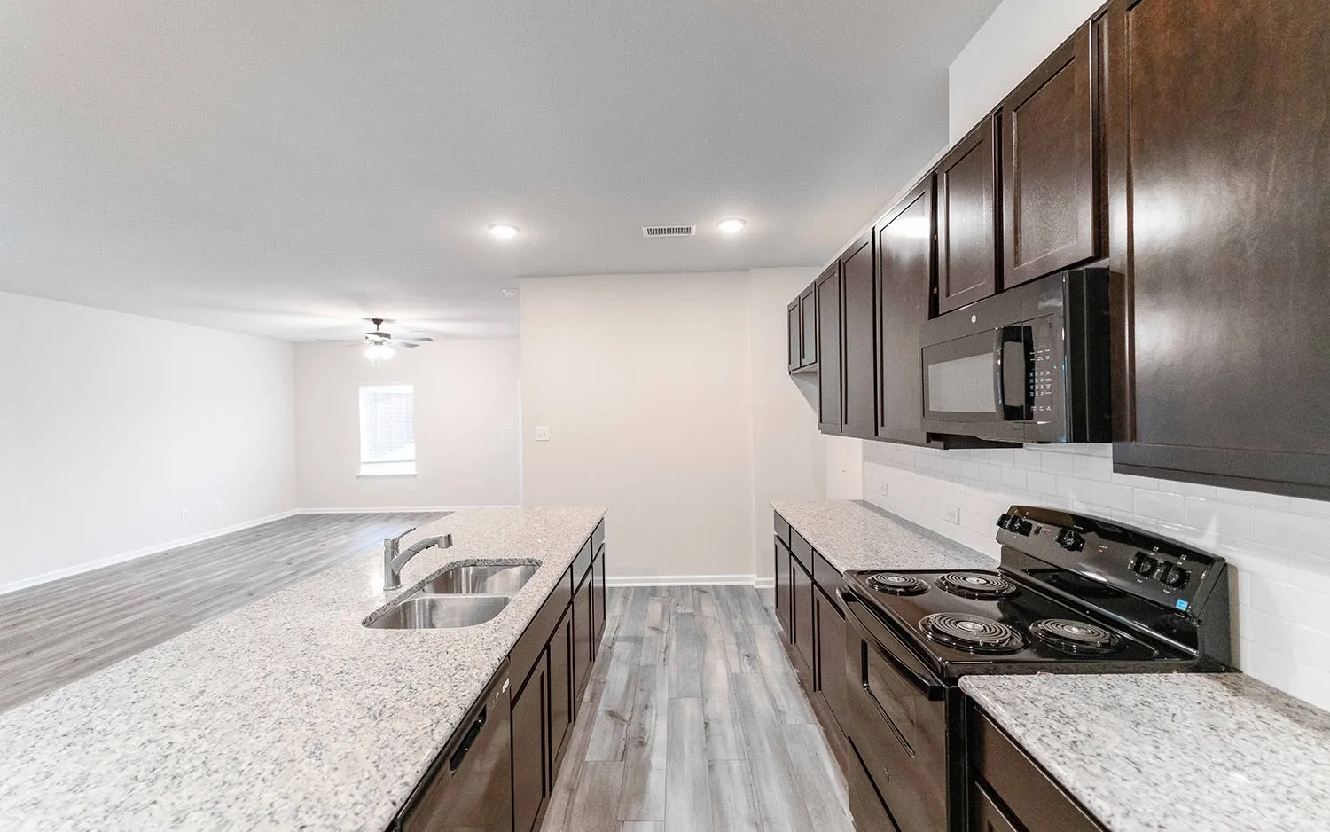 Spacious open-concept kitchen featuring dark wood cabinetry, light speckled countertops, a built-in microwave, and a black electric range
