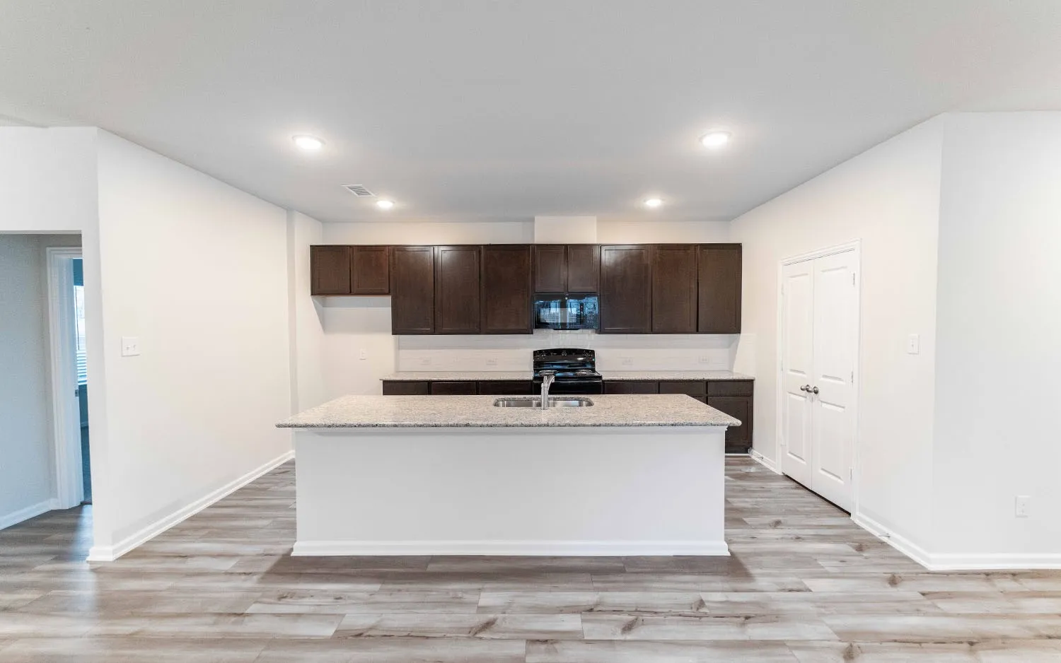 Kitchen island with a built-in sink, stone-finish countertop, dark wood-finish cabinetry, and wood-finish flooring