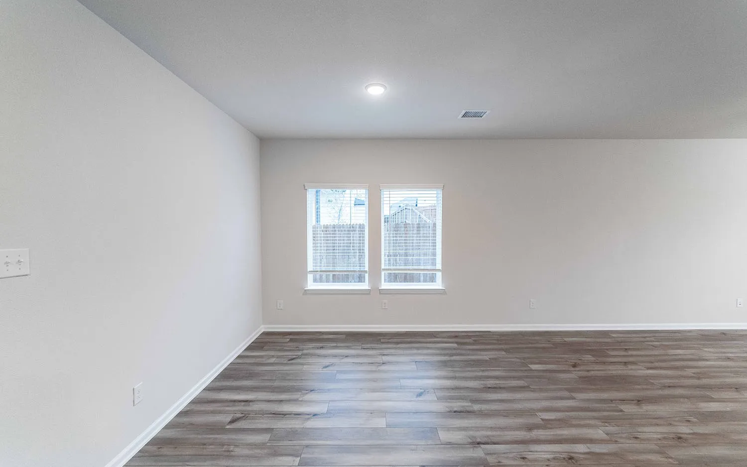 Spacious room featuring wood-finish flooring, light-colored walls, recessed ceiling lighting, and a single window with blinds