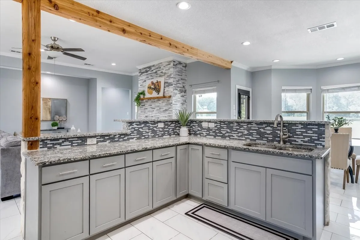 Kitchen featuring light gray cabinetry, speckled countertops, a mosaic tile backsplash, and a stainless steel sink with a gooseneck faucet