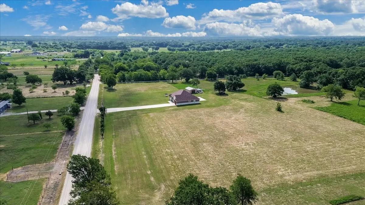 Expansive acreage featuring a single-story residence with a brown roof, a private pond, mature trees, and a paved driveway