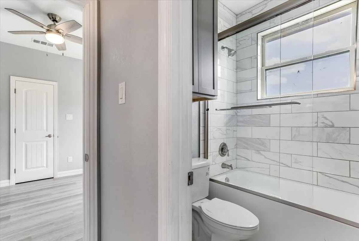 Bathroom featuring a tiled tub and shower combination with a window, complemented by a light gray cabinet
