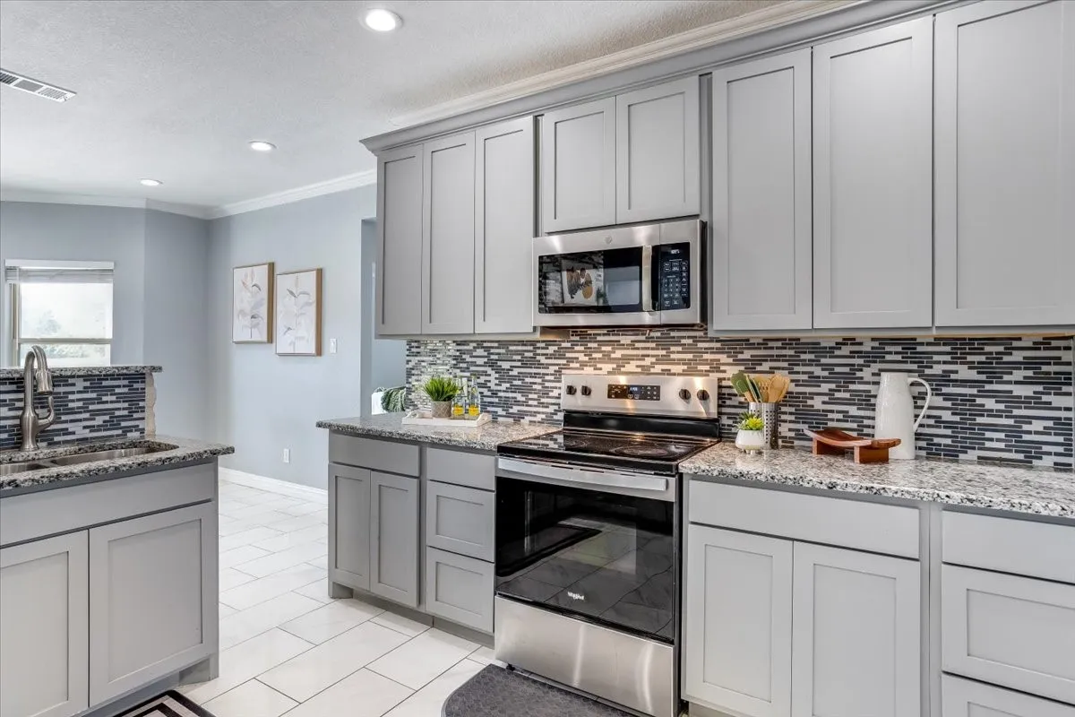 Kitchen featuring light gray cabinetry, stainless steel appliances, granite countertops, and a mosaic tile backsplash