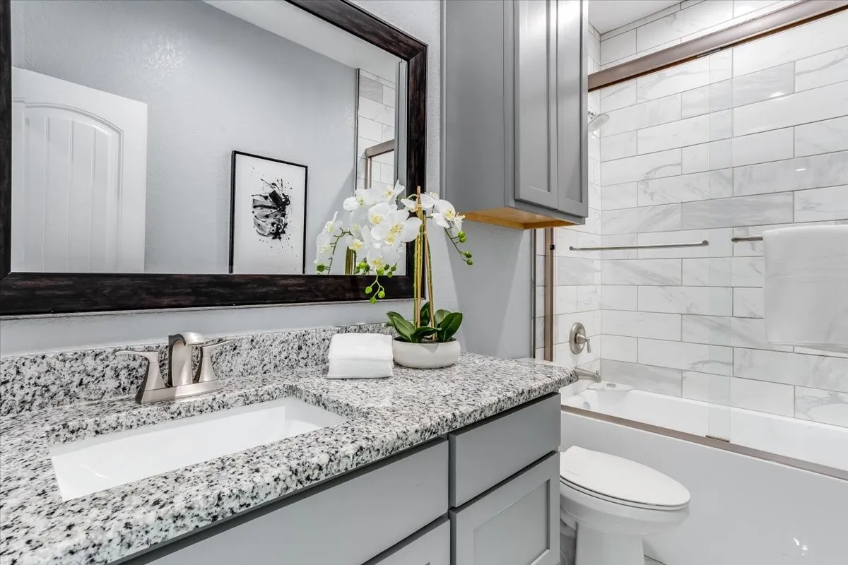 Bathroom vanity featuring a granite countertop with an undermount sink, brushed nickel faucet, and frameless mirror
