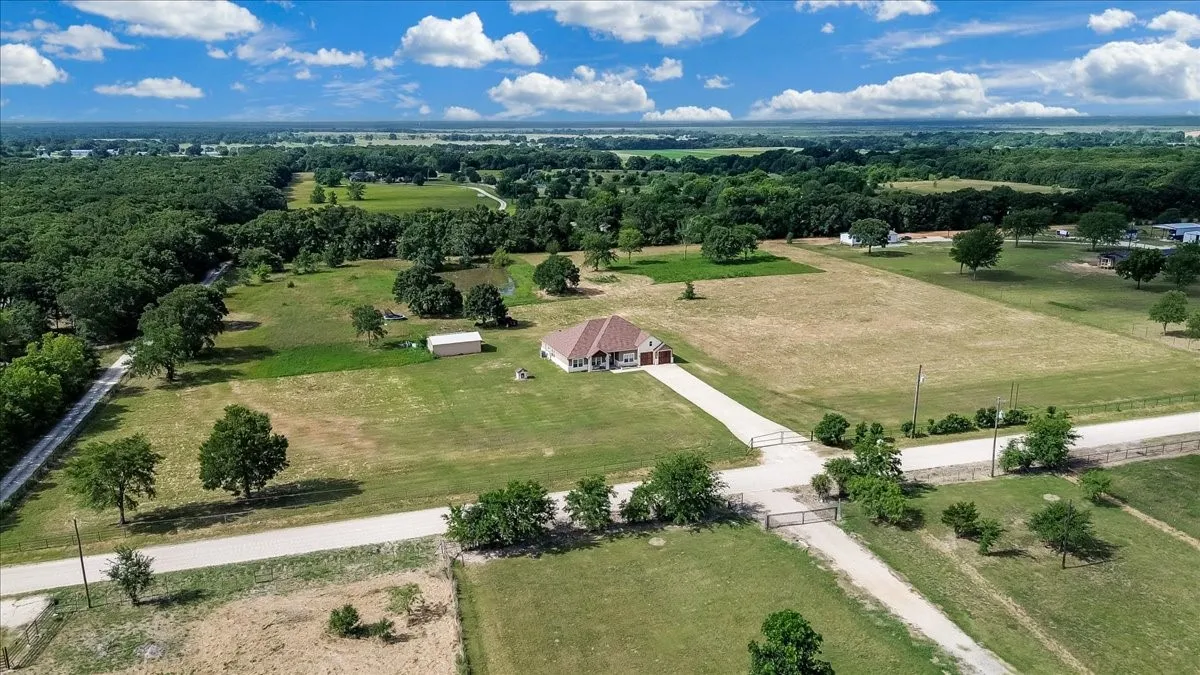 Expansive rural property featuring a single-story residence with an attached two-car garage, long paved driveway, and gated entry