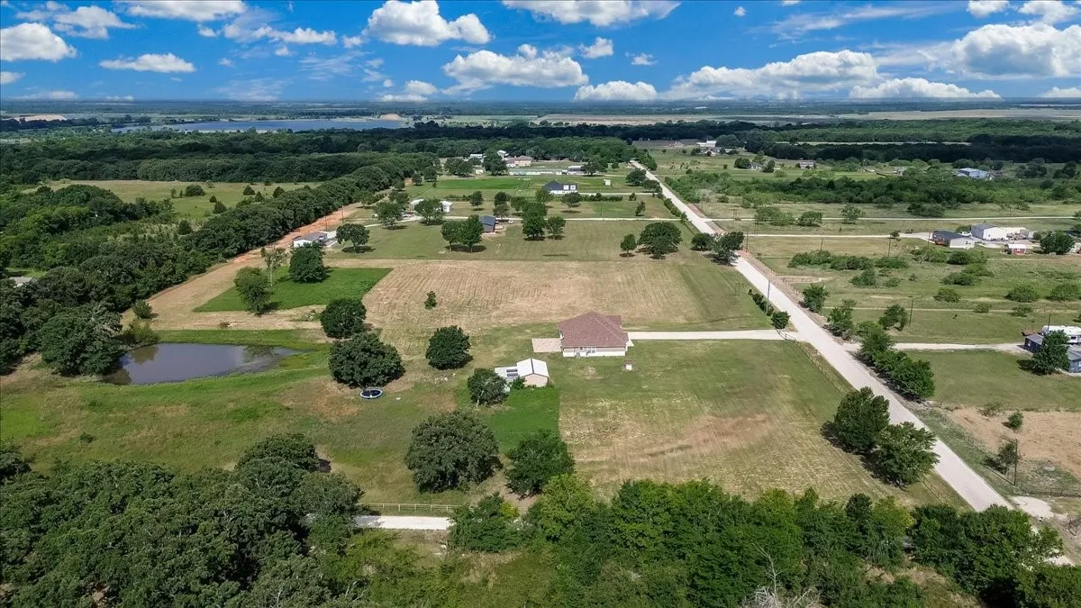 Expansive rural property featuring a brown-roofed residence, a private pond, mature trees, and a paved road frontage