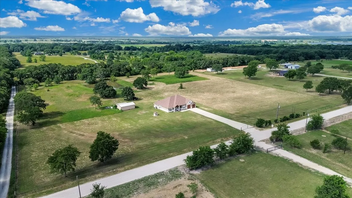 Expansive rural property featuring a central residence with a detached outbuilding, extensive paved driveway, and established perimeter fencing