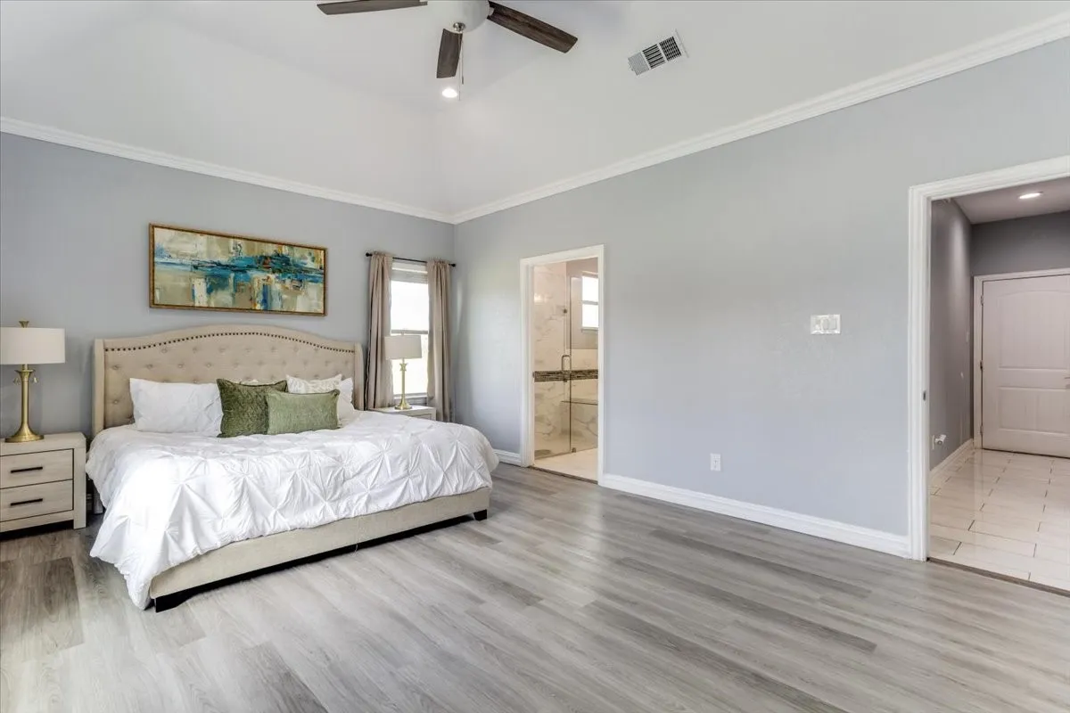 Spacious room featuring vaulted ceilings, light wood-finish flooring, and crown molding