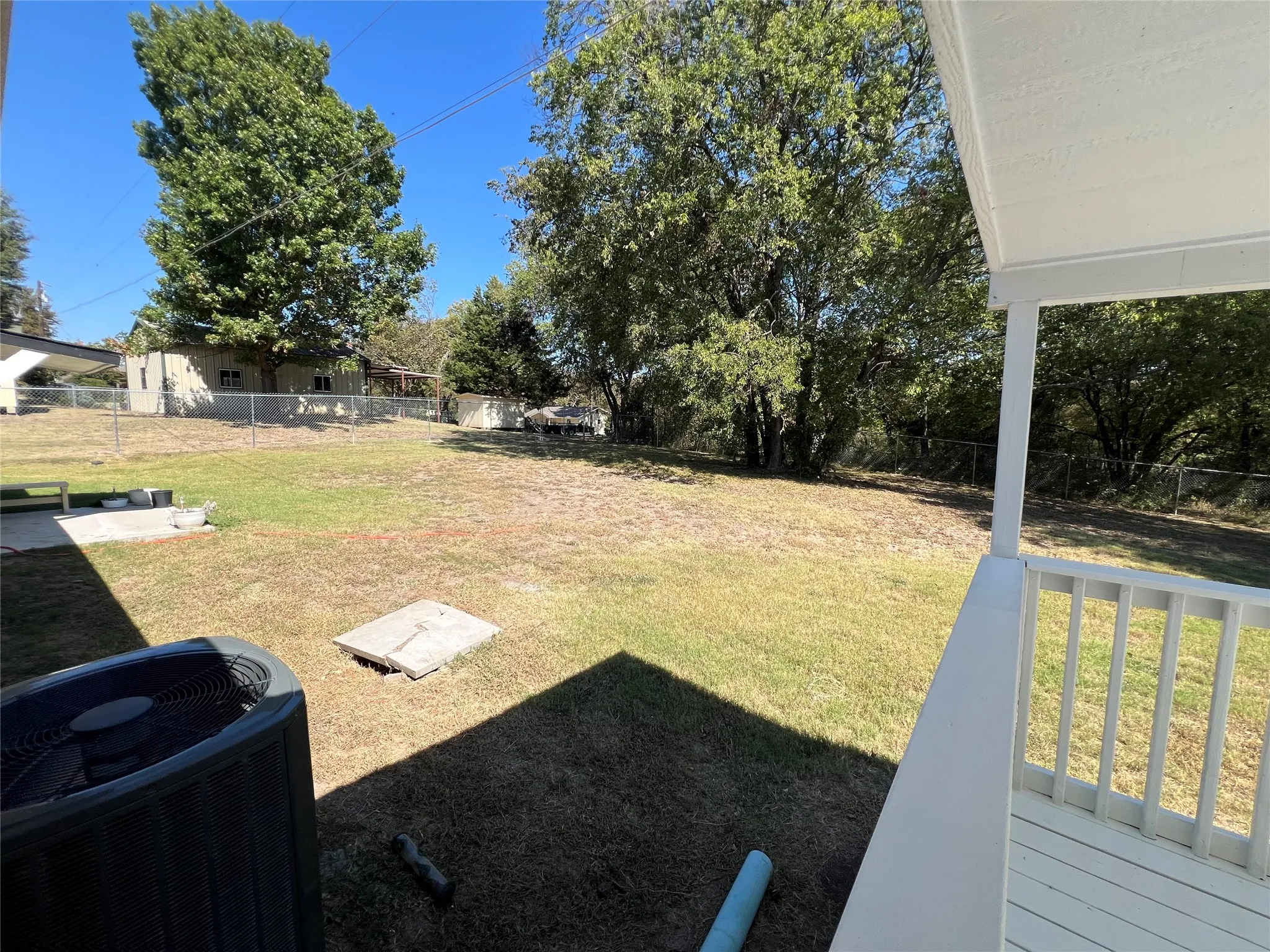Spacious backyard featuring a chain-link fence, mature trees, and an air conditioning unit