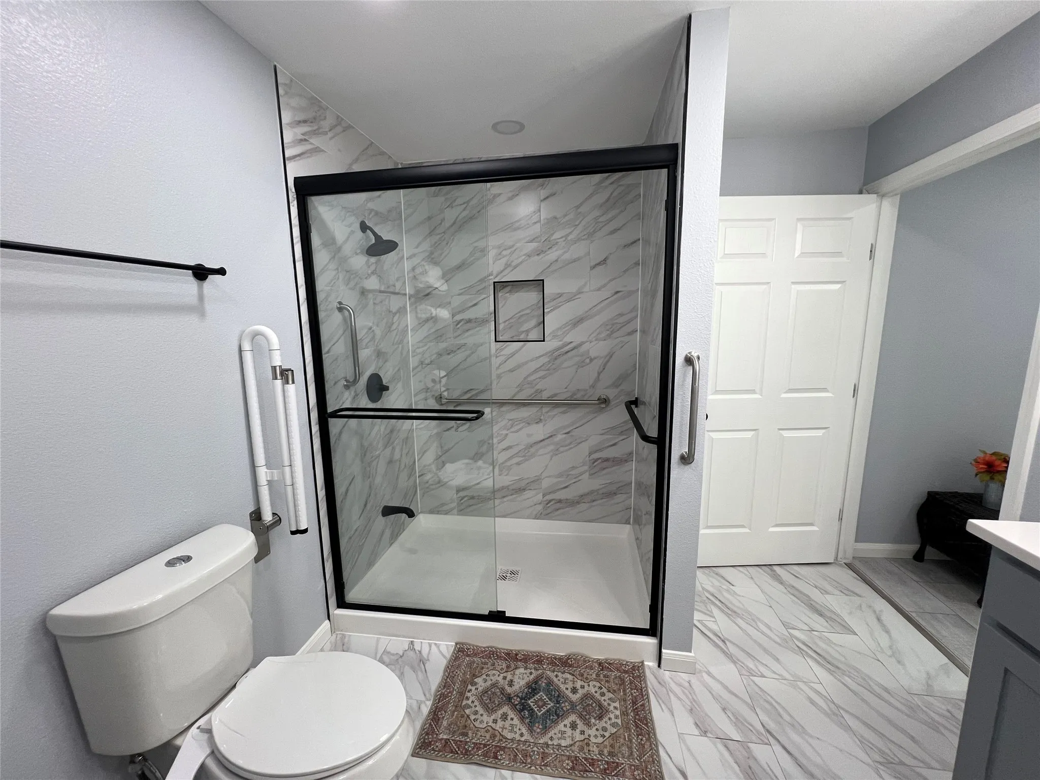 Walk-in shower with black-framed glass enclosure, integrated shelving, and multi-setting showerhead