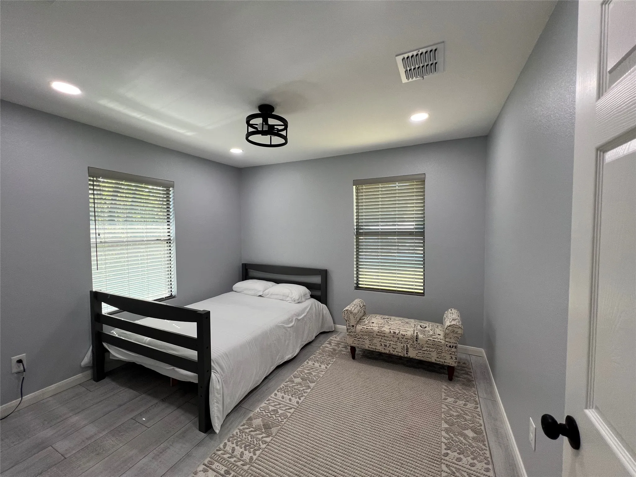Interior room featuring wood-finish flooring, two windows with blinds, a black ceiling fan, and recessed lighting