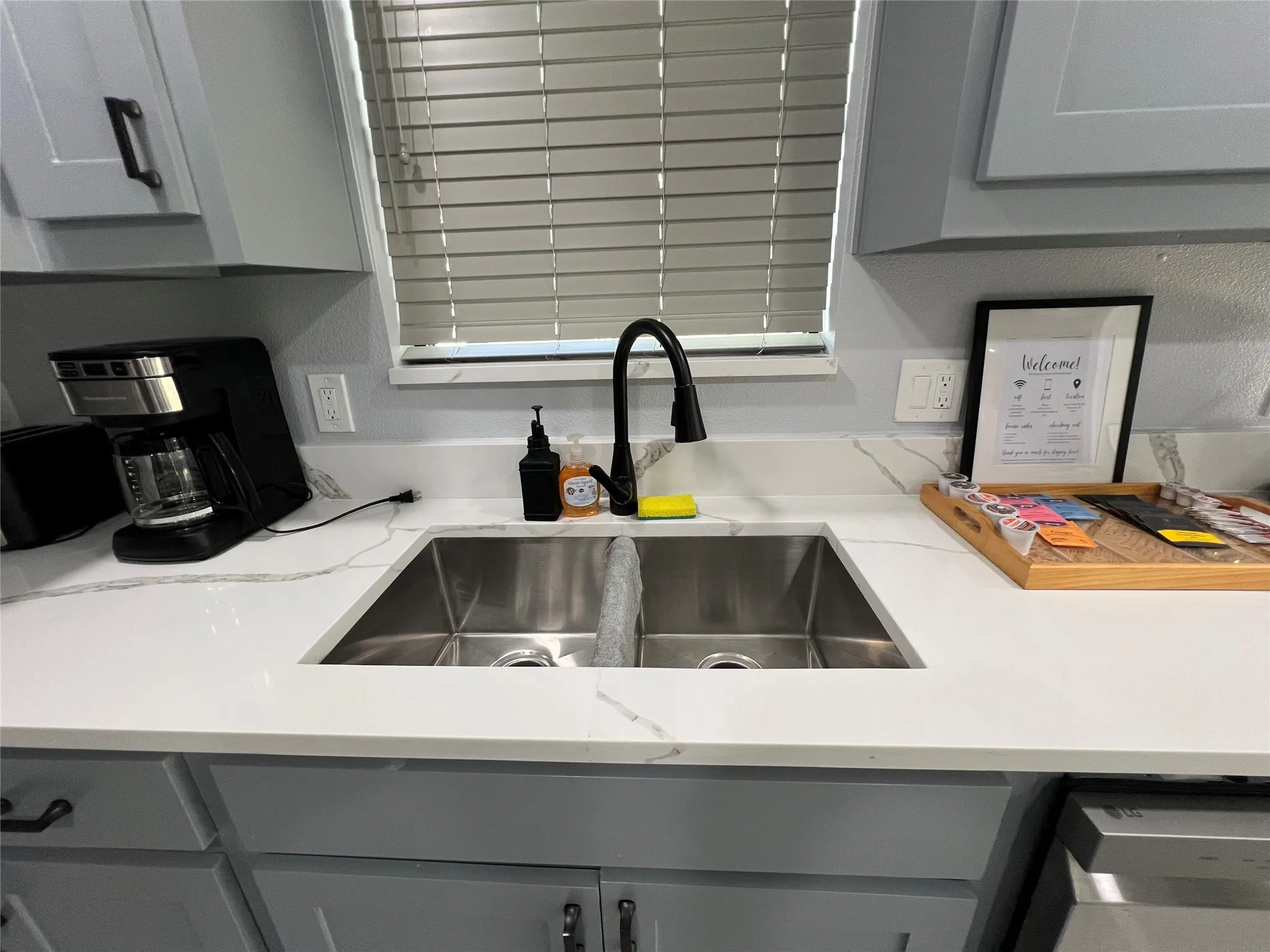 Dual stainless steel sink with a matte black faucet, set within white countertops featuring subtle gray veining