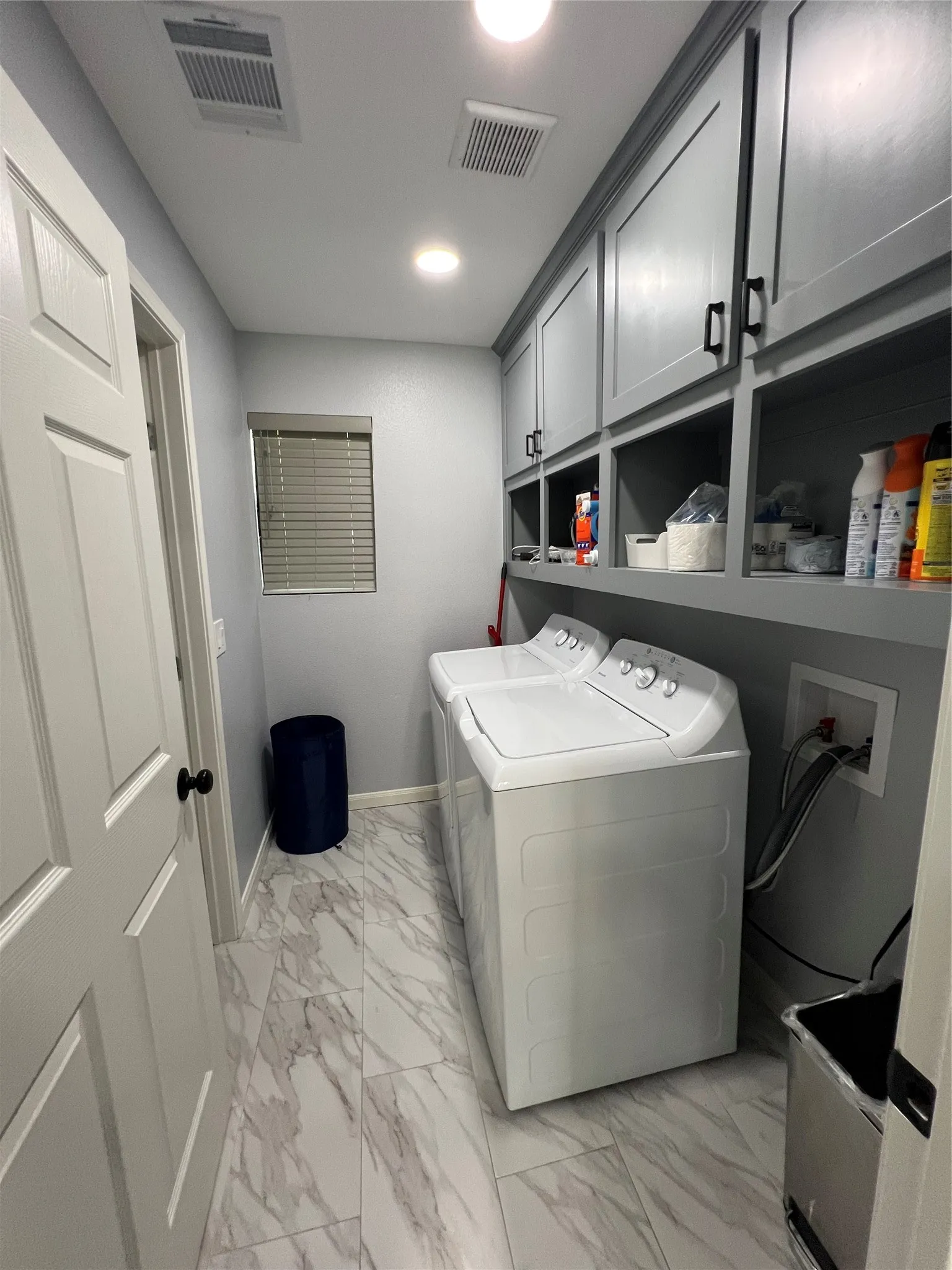 Dedicated laundry area featuring slate gray shaker-style cabinetry with matte black hardware, recessed lighting, and rectangular marble-look floor tiles