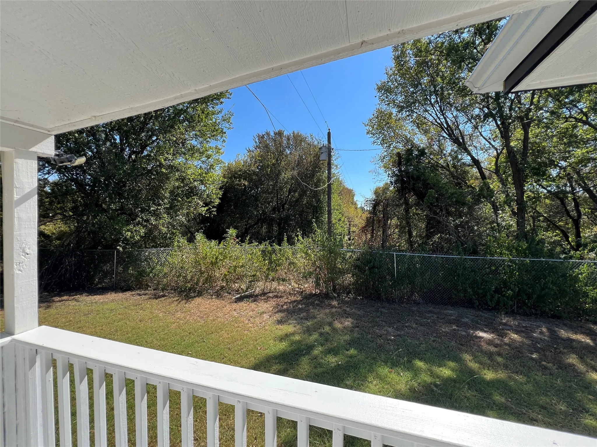 Covered porch with white railings overlooking a fenced backyard with mature trees