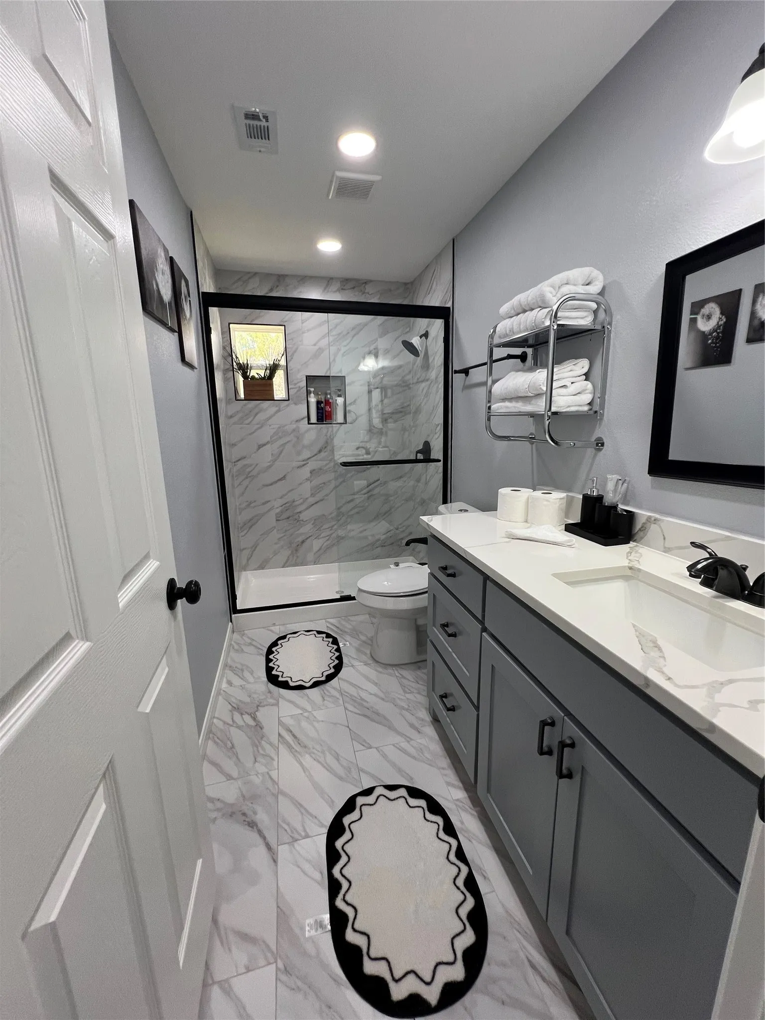 Bathroom featuring a glass-enclosed shower with white marble-style tile surround and recessed shelving