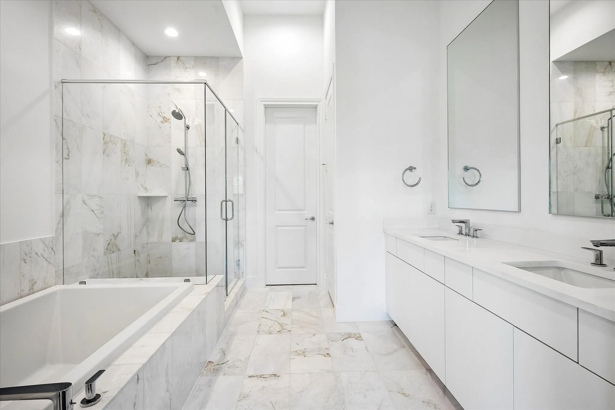 Bathroom featuring a full-length tub, glass-enclosed shower, dual vanity with undermount sinks, and tiled flooring