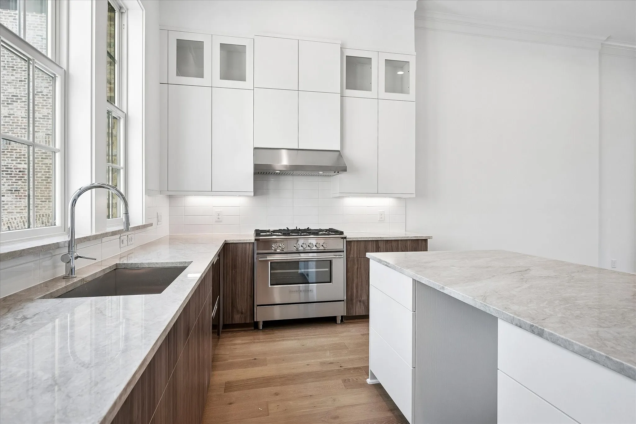 Bright kitchen featuring an integrated gas range, stainless steel appliances, a deep basin sink, and a large central island