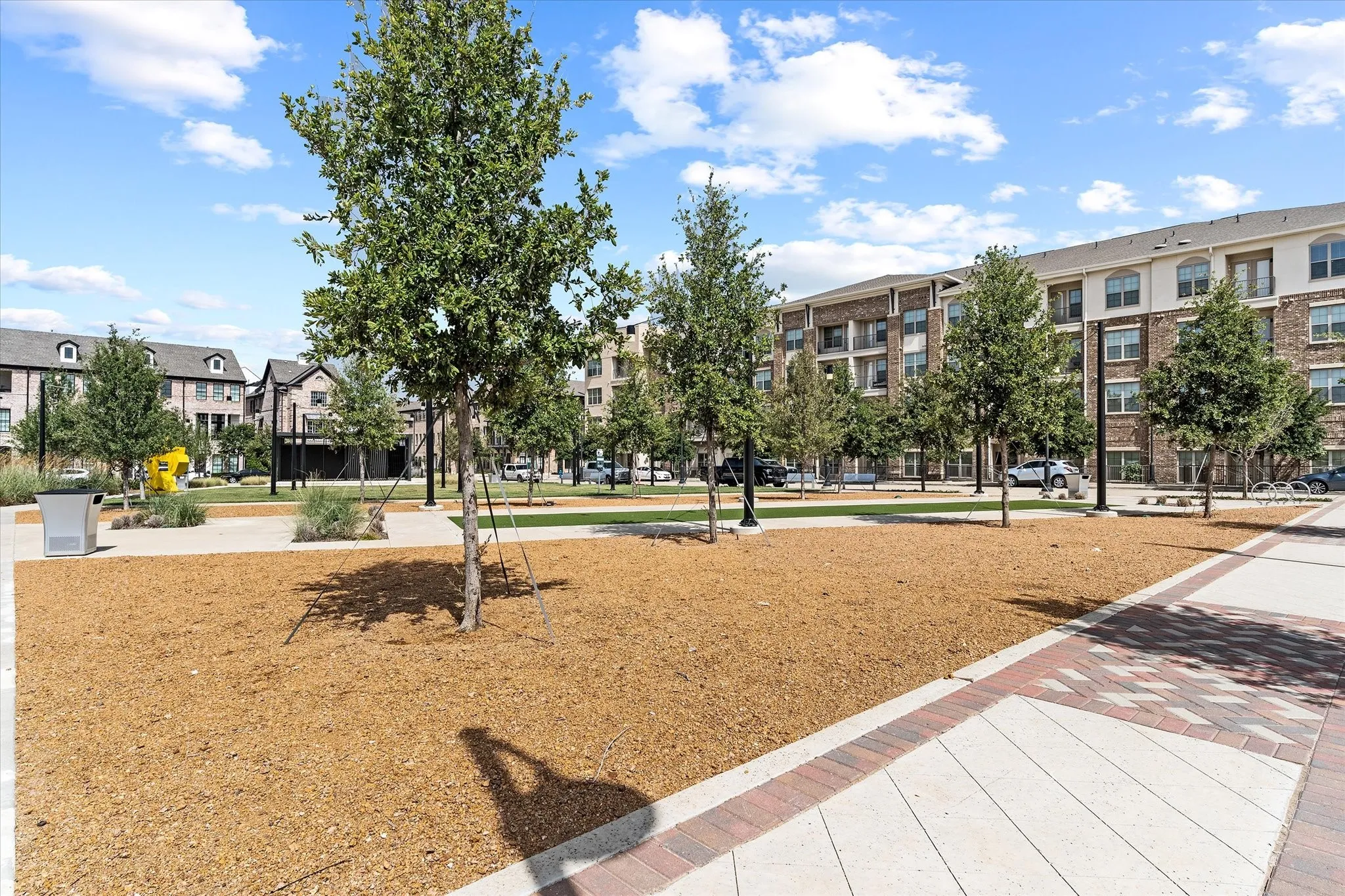 Expansive common area featuring a central wood chip ground cover, mature trees, and patterned hardscaping