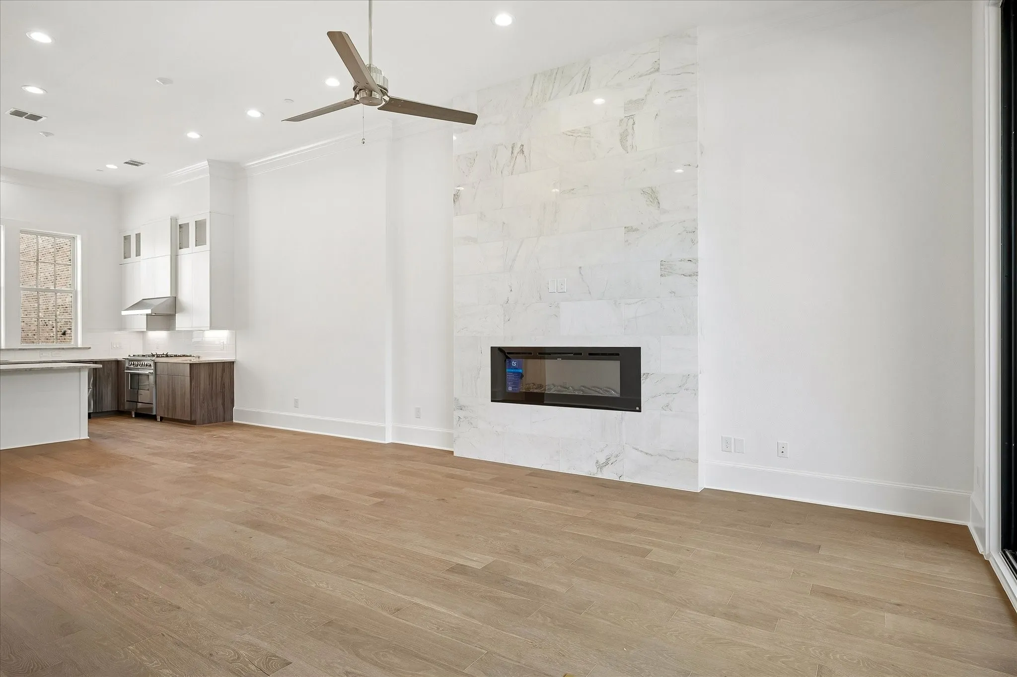 Open-concept living area with wood-finish flooring, a contemporary fireplace with a large-format tile surround, recessed lighting, and a ceiling fan
