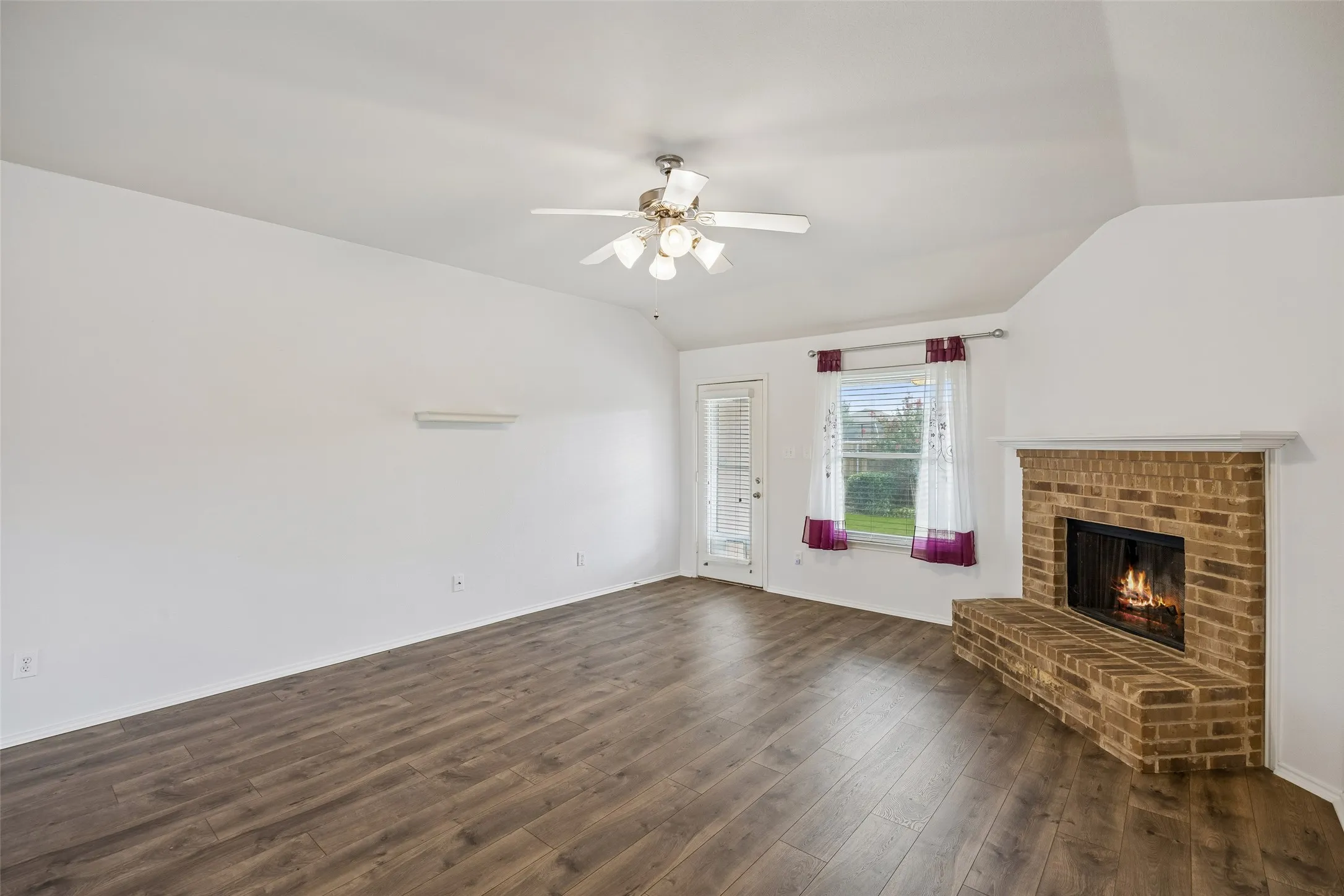 Designed for both comfort and entertaining, the spacious living room features beautiful new flooring, vaulted ceilings, a cozy brick fireplace, and convenient backyard access.