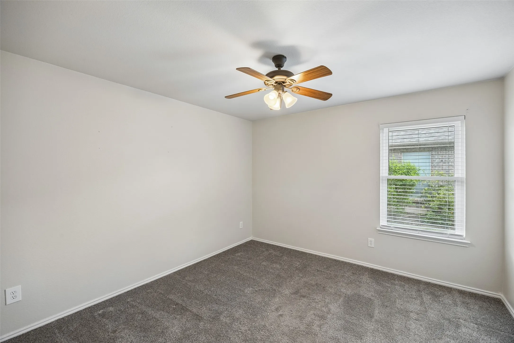 The third bedroom offers a spacious layout with plush carpeting, a ceiling fan, and a bright window that fills the room with natural light.