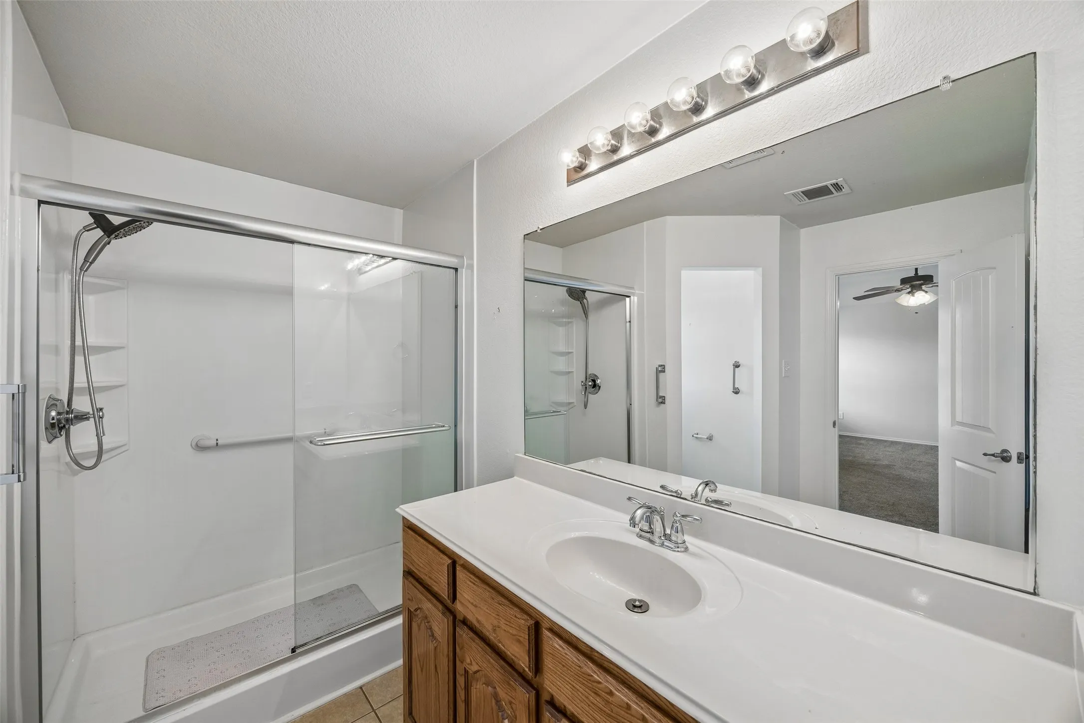The primary bathroom offers an oversized vanity, glass-enclosed walk-in shower with grab bars, and a comfort-height toilet for added accessibility and convenience.