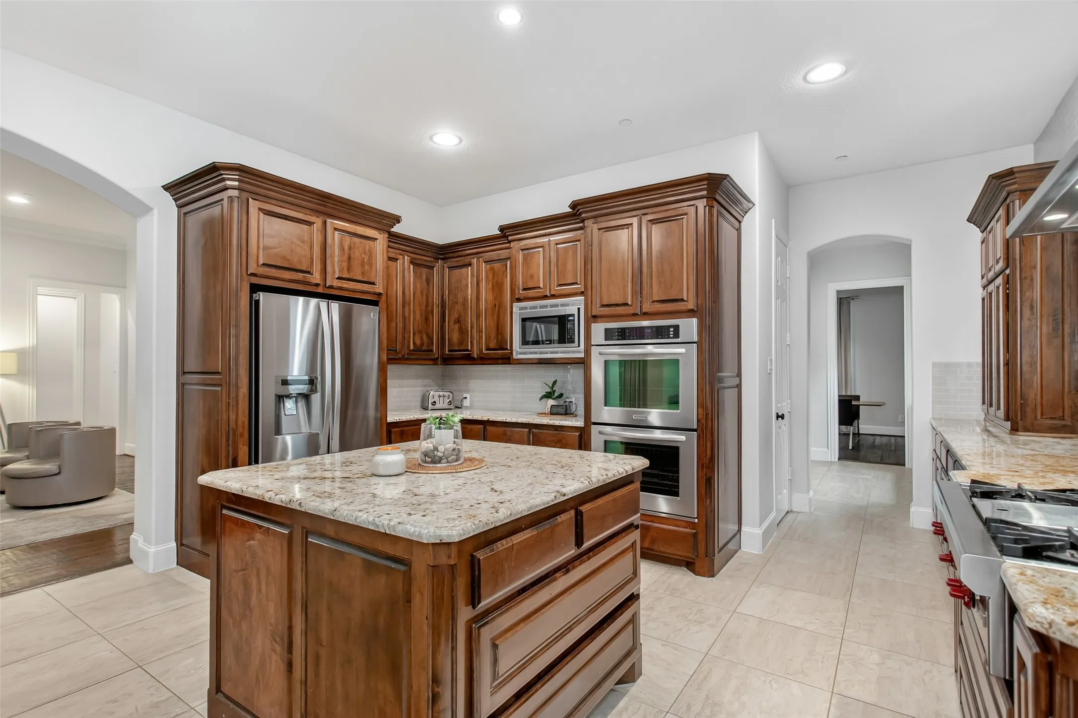Spacious kitchen featuring an expansive island with a light-toned countertop, rich wood cabinetry, stainless steel appliances, and large format floor tiling