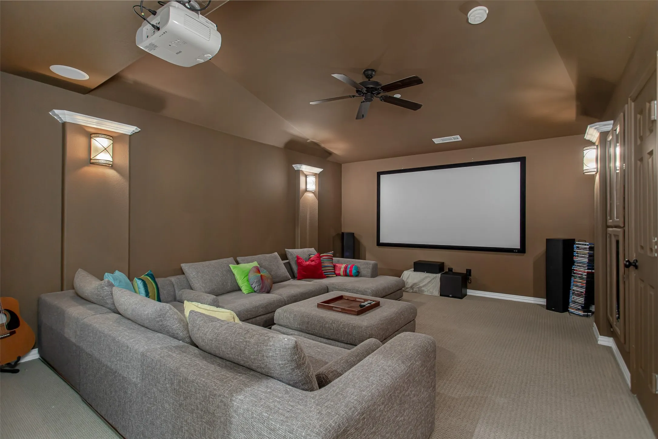 Dedicated media room featuring a large projection screen, mounted projector, and a ceiling fan